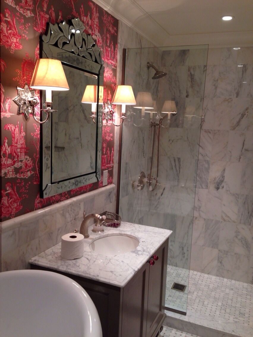 Dramatic bathroom with Pink wallpaper, ornate mirror, wall sconces, and marble shower wall