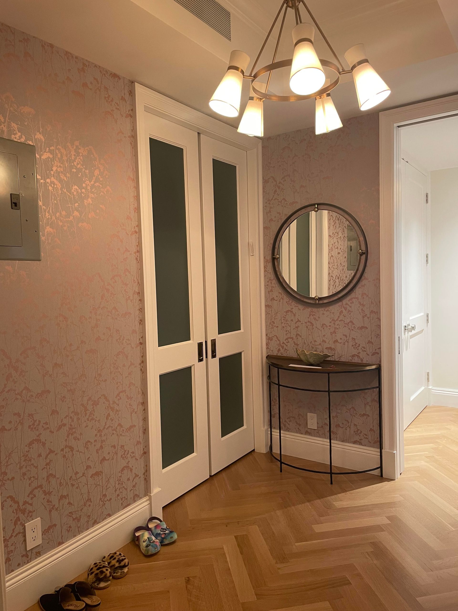 Foyer area with round mirror, patterned wallpaper, and multi-light fixture