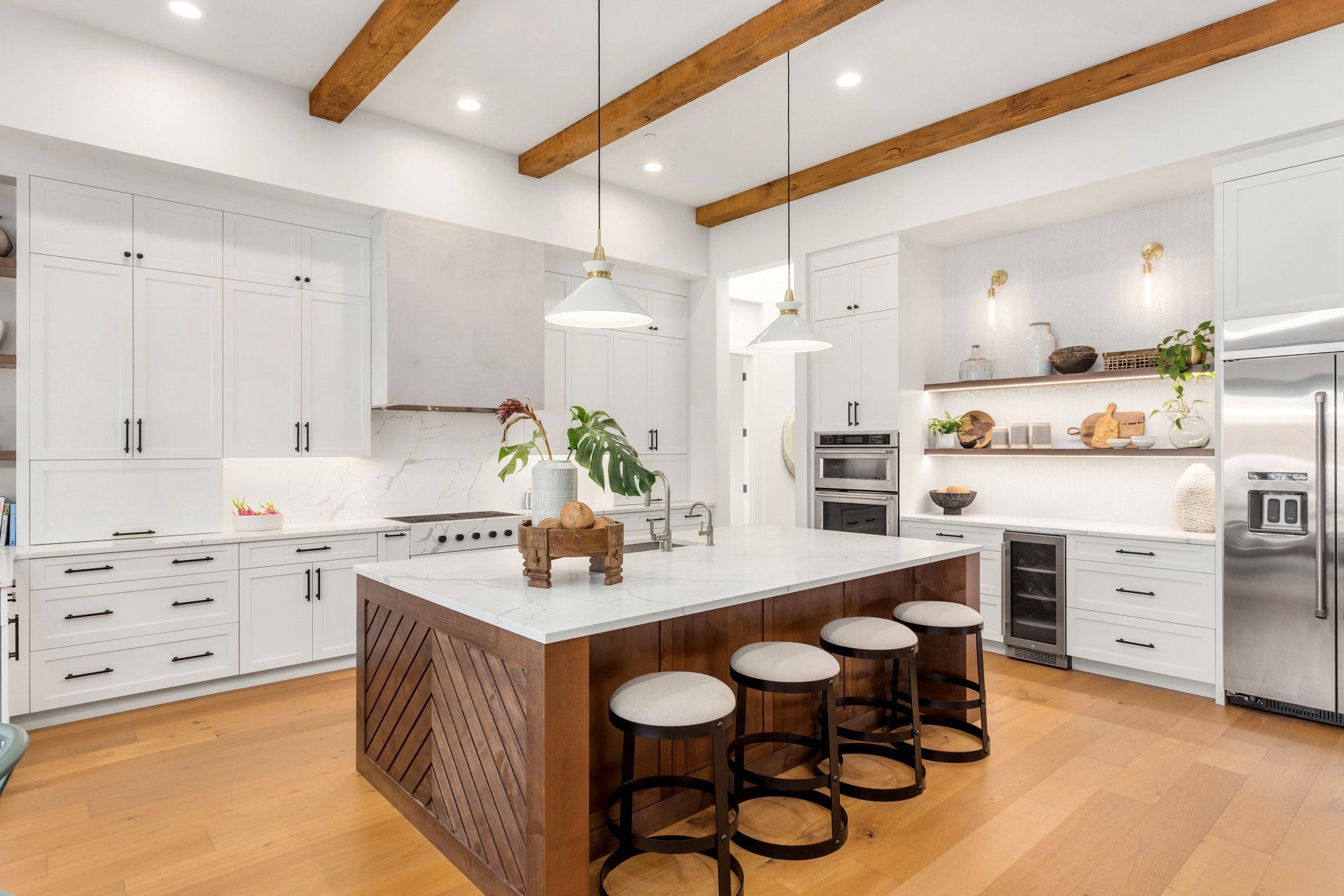 Una cocina con muebles blancos, pisos de madera, taburetes y una gran isla.