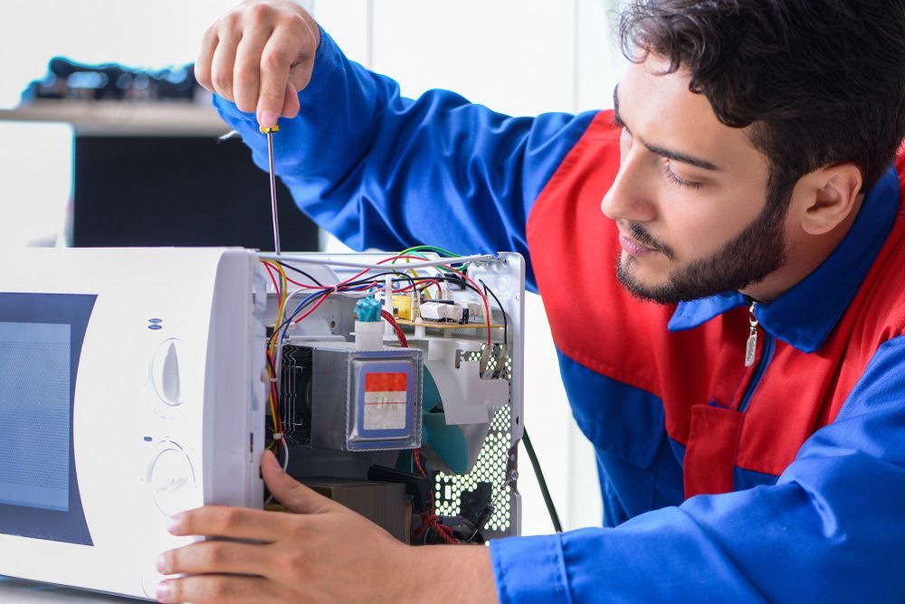 A Man Is Fixing A Microwave Electric Wiring With A Screwdriver — Appliance City in Lake Cathie, NSW