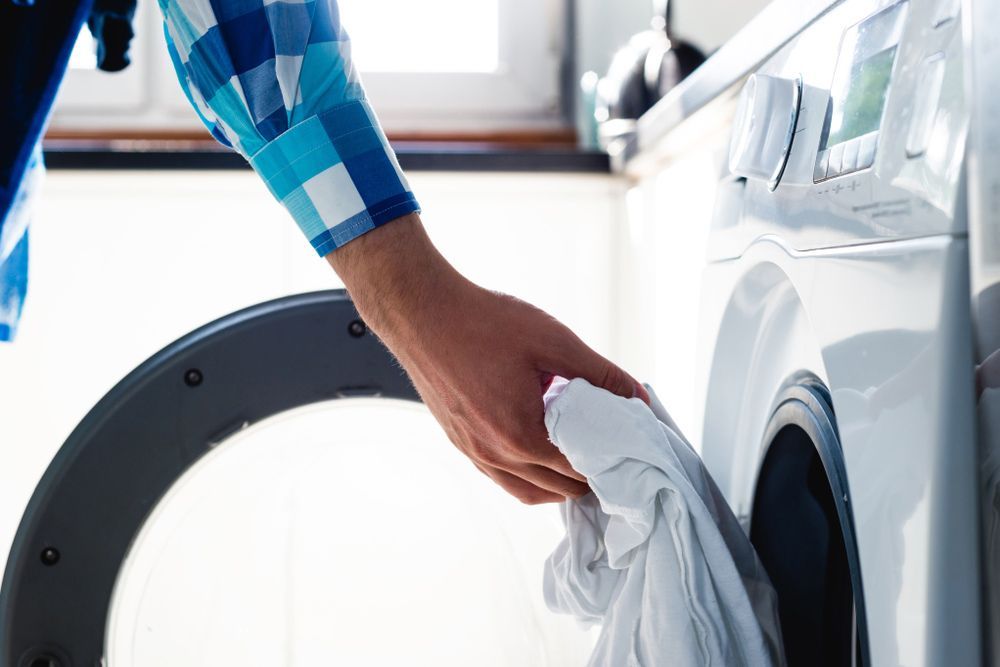A Man Is Putting Clothes In A Washing Machine — Appliance City in Port Macquarie, NSW