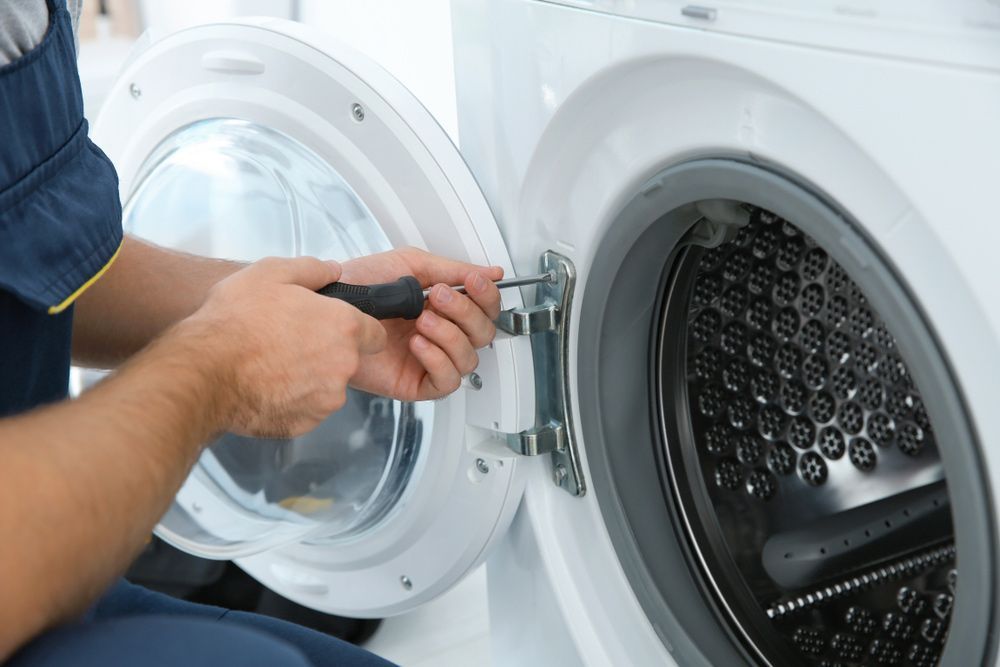 A Man Is Fixing A Washing Machine Door With A Screwdriver — Appliance City in Port Macquarie, NSW