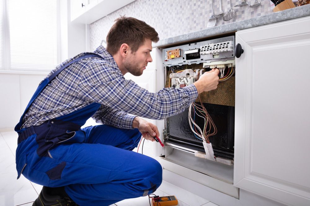 A Man Is Repairing A Dishwasher Circuit Board In A Kitchen — Appliance City in Port Macquarie, NSW