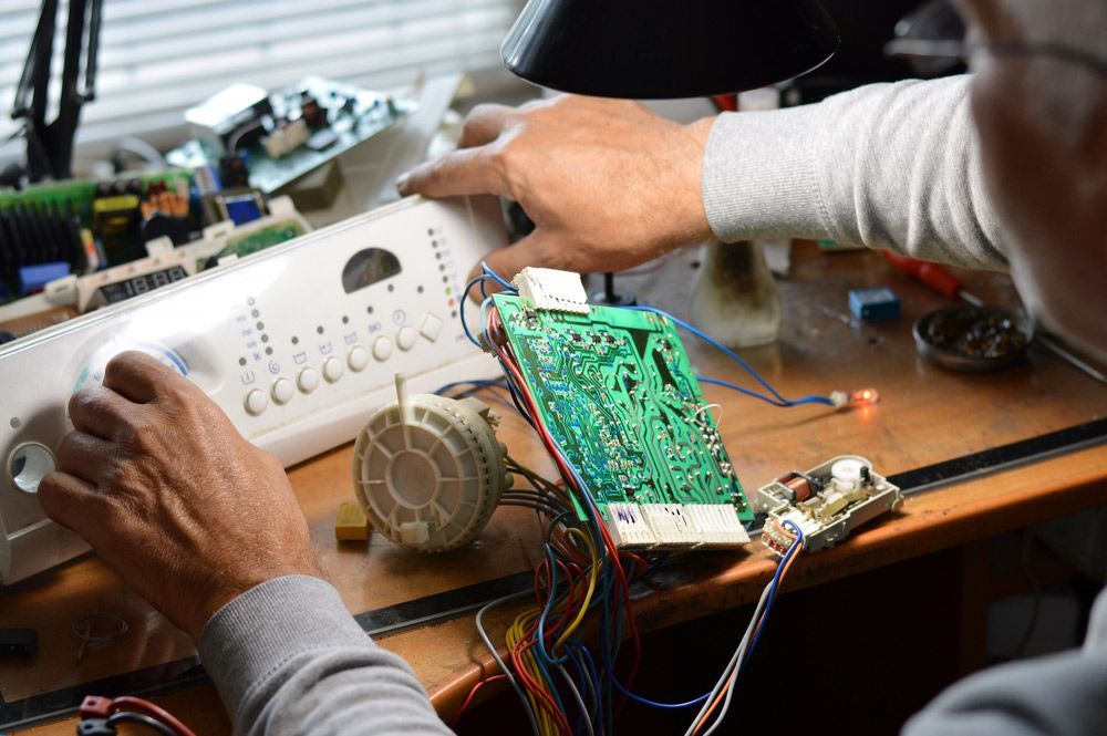 A Man Is Working On A Washing Machine Electric Circuit Board On A Desk — Appliance City in Port Macquarie, NSW