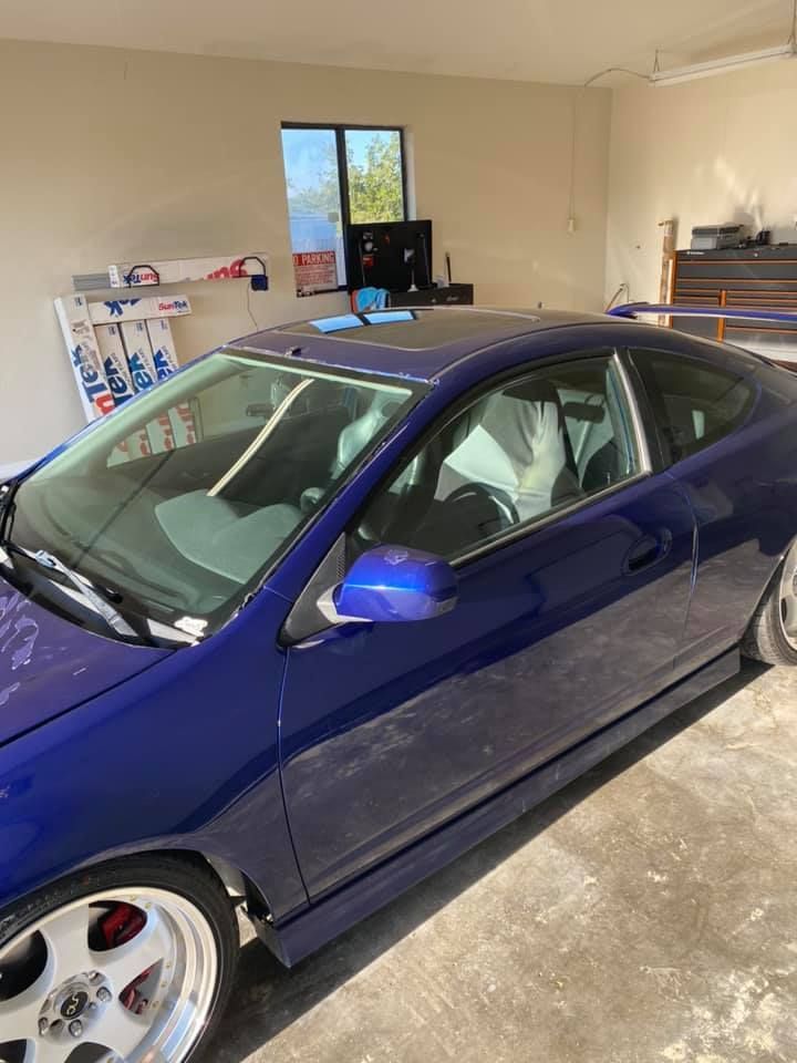 Blue sports car parked inside a garage. It has a spoiler, custom wheels, and red brake calipers.