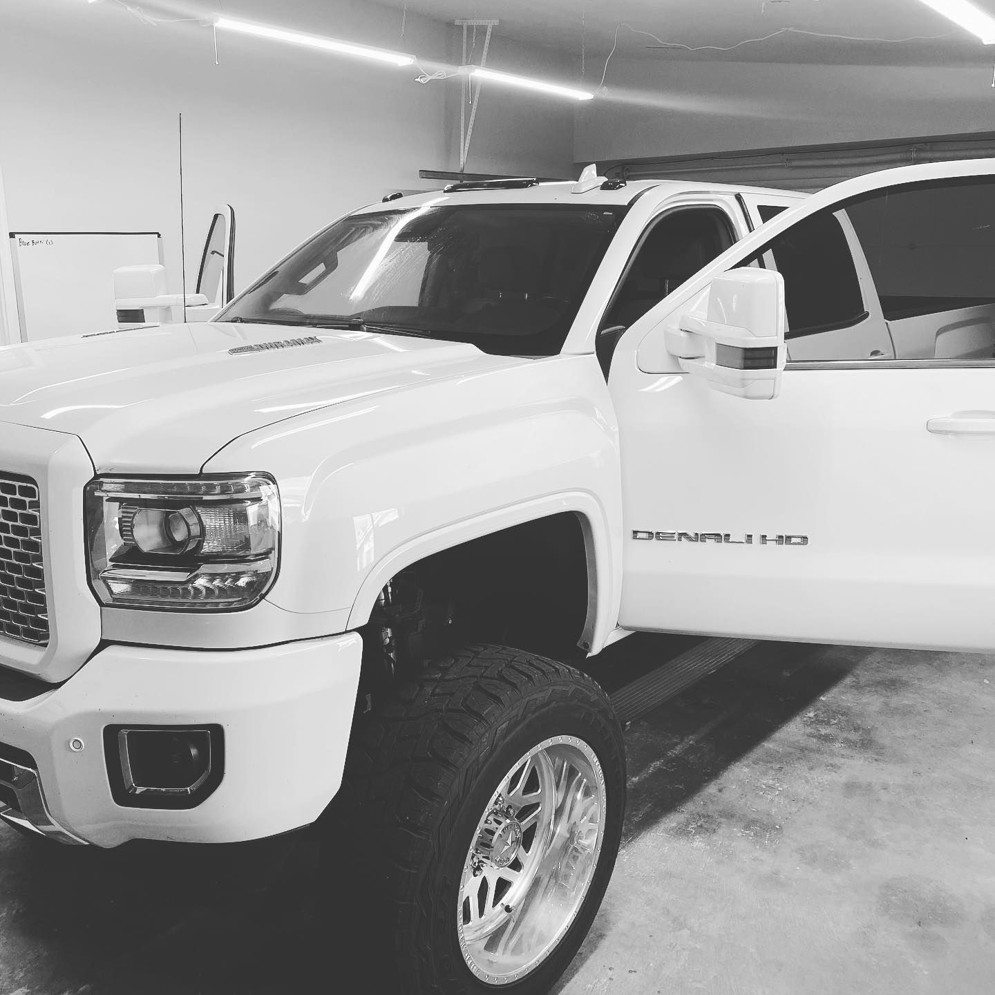 White GMC Denali truck with lifted suspension and open door in a garage.