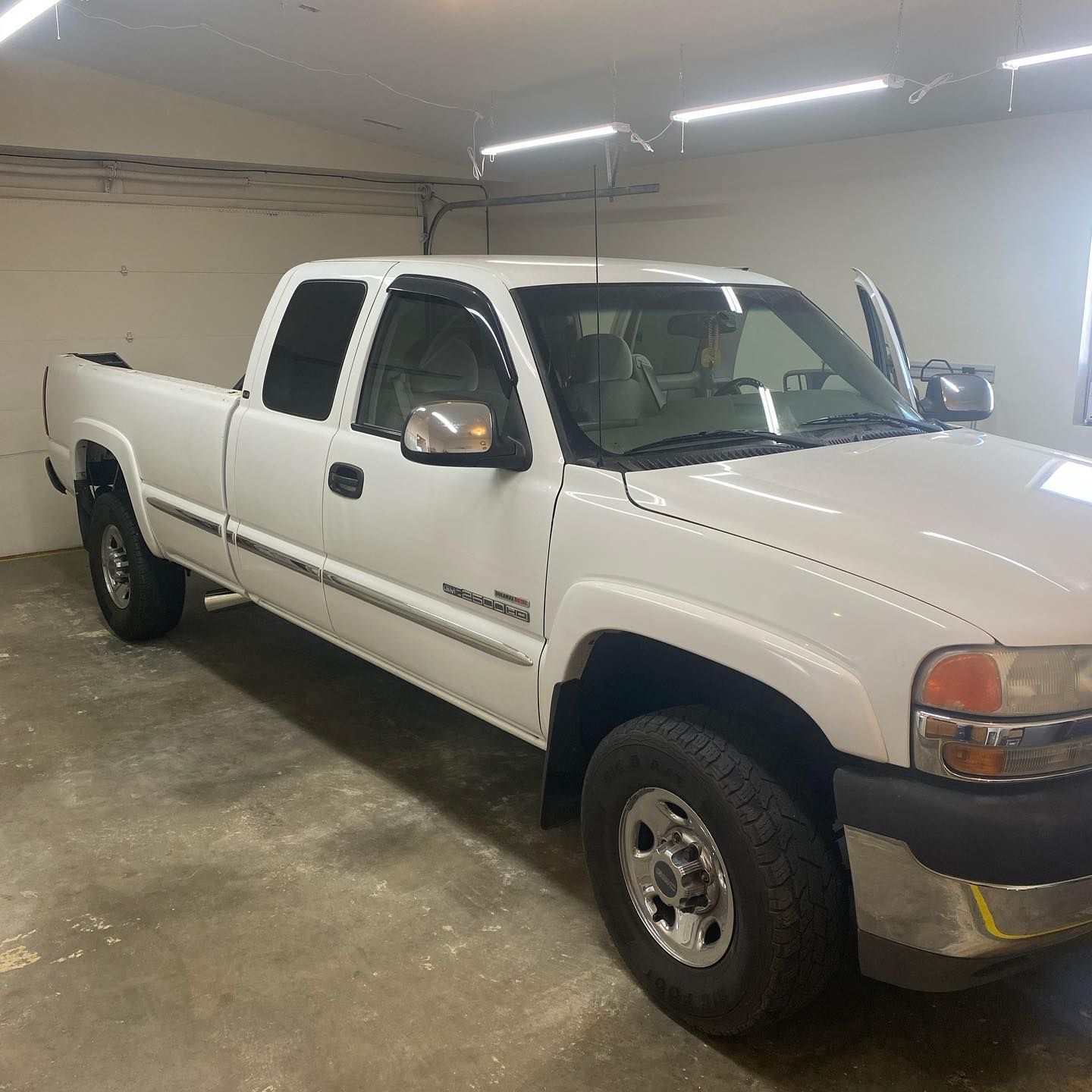A white Chevrolet Silverado pickup truck parked inside a garage. The driver's side door is open.