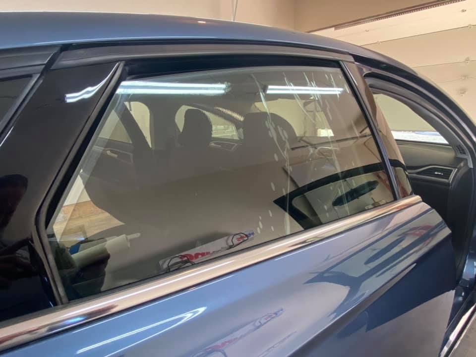 Blue car window with tint film applied, interior visible with seats. The window is framed with black trim.