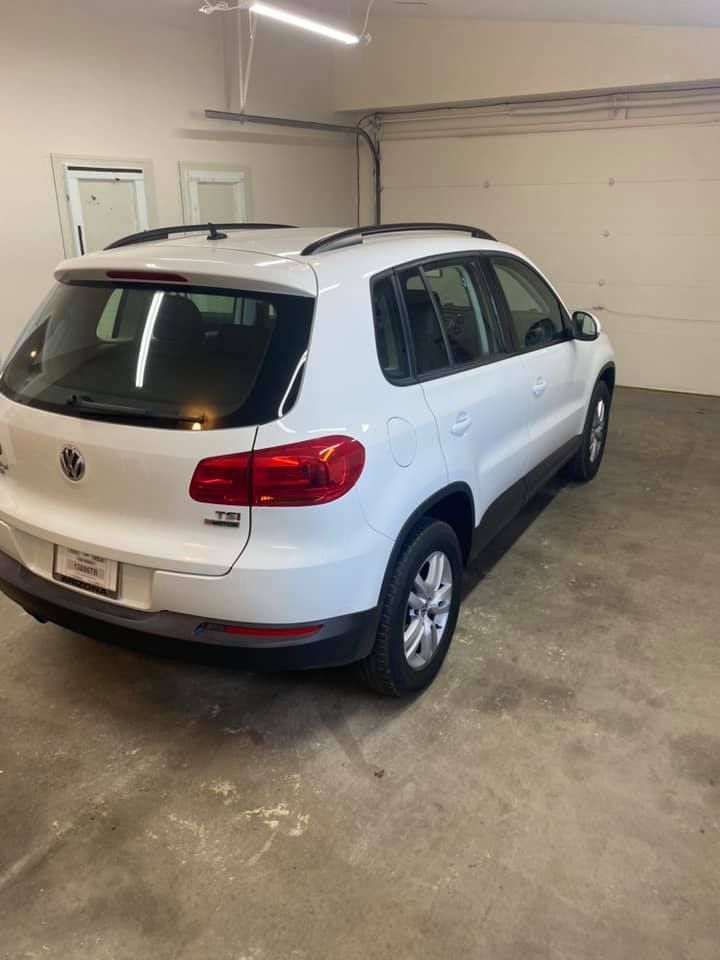 White Volkswagen Tiguan SUV parked inside a garage. The vehicle's rear and side are visible.