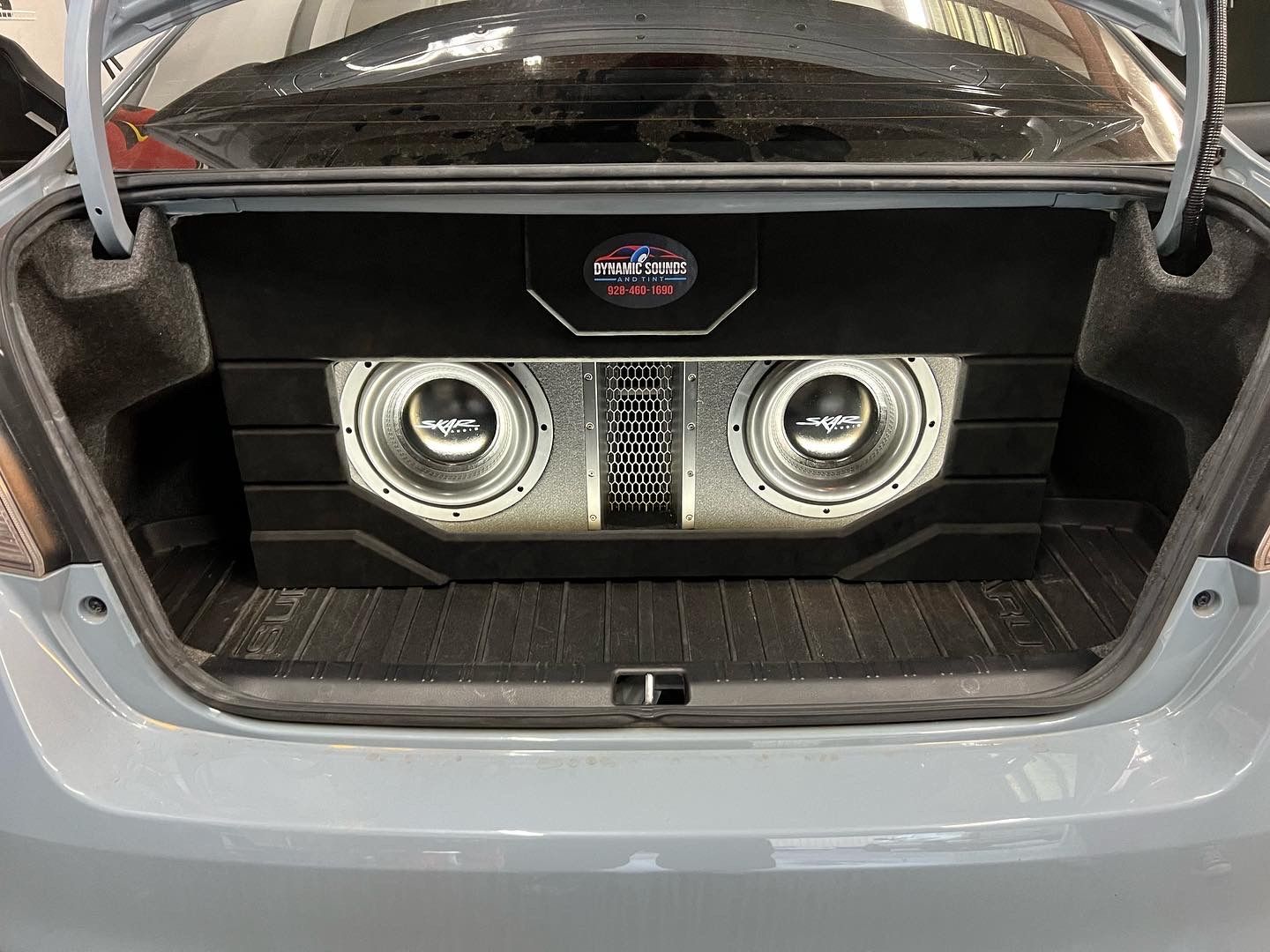 Car trunk with custom audio system featuring two subwoofers and a central amplifier, illuminated by bright lights.