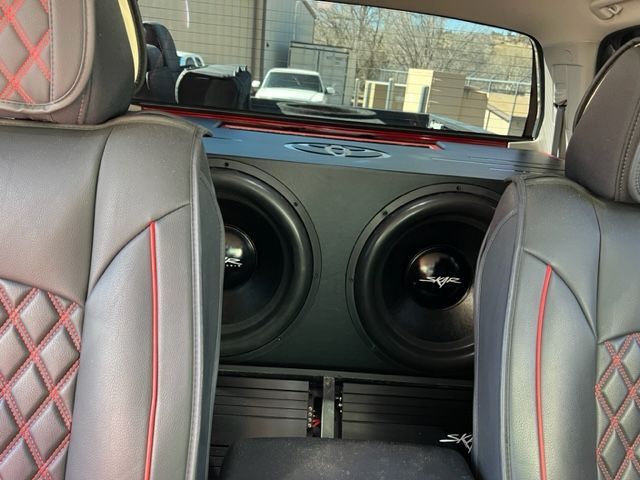 Backseat view of a car interior with custom red-stitched seats and a large speaker box with two woofers.