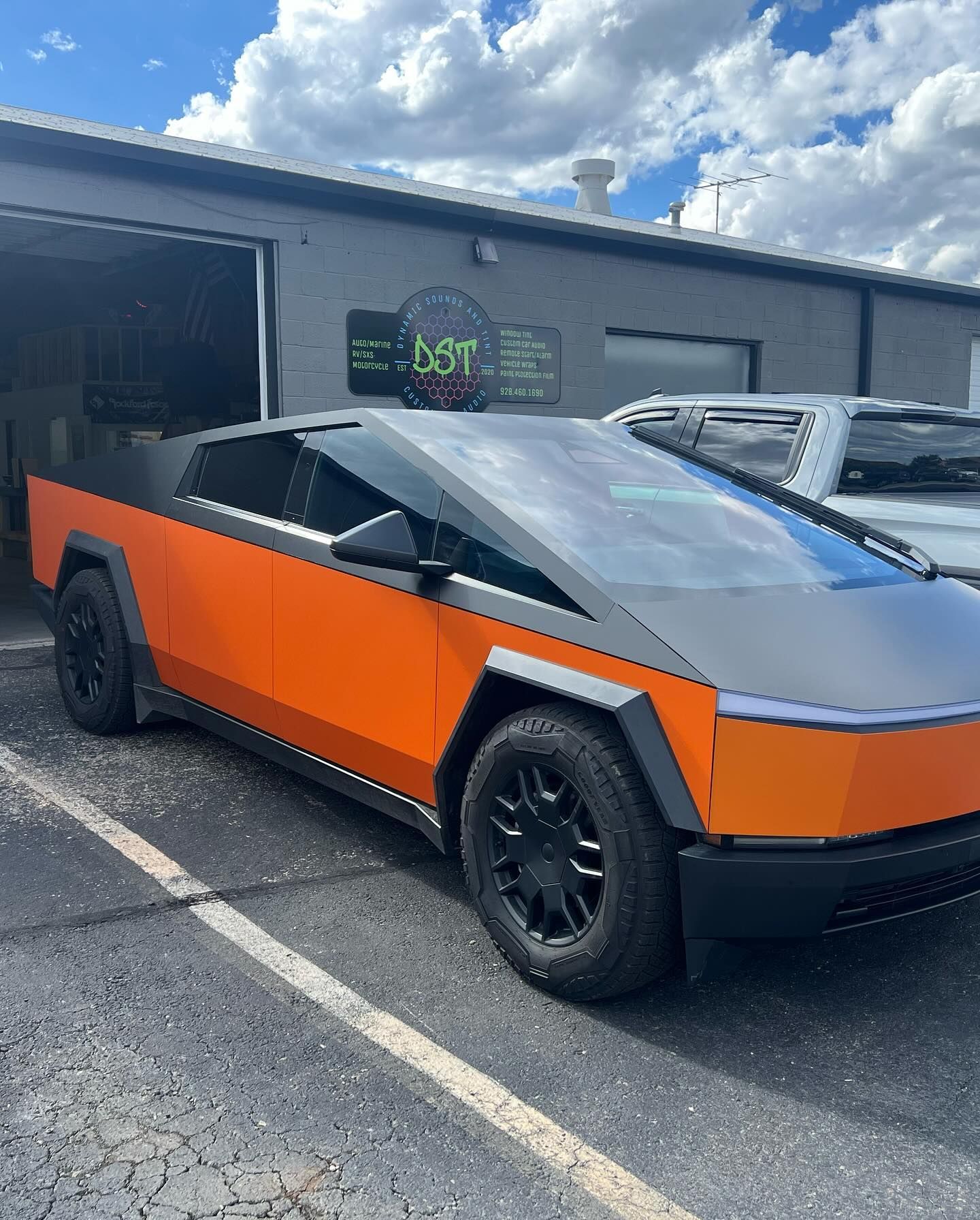 Tesla Cybertruck in an orange wrap with black accents parked in front of a business on a sunny day.