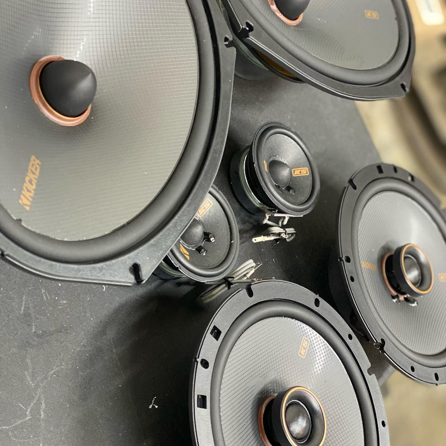 Car audio speakers, including large woofers and smaller tweeters, arranged on a surface.  The speakers are black and have copper-colored accents.