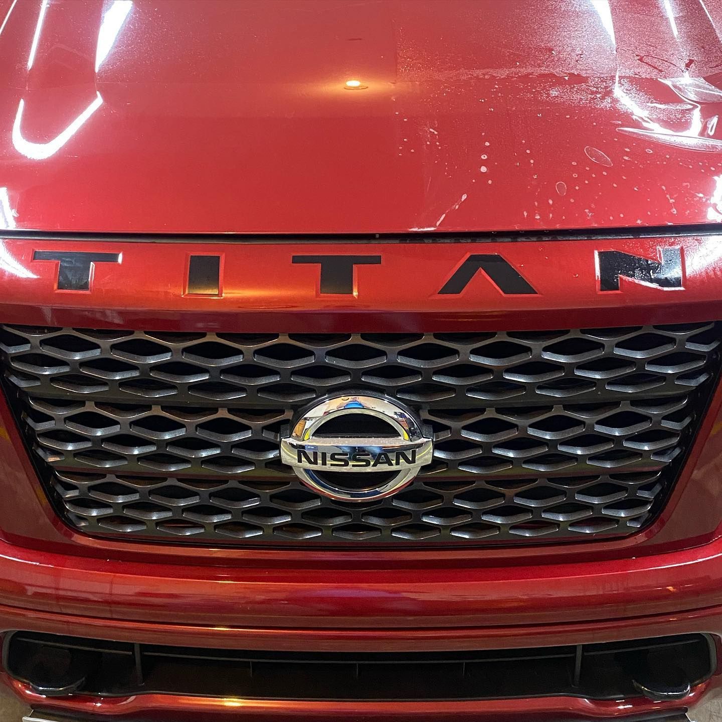 Close-up of a red Nissan Titan truck's front grill, featuring the Titan name above the grill and the Nissan logo.