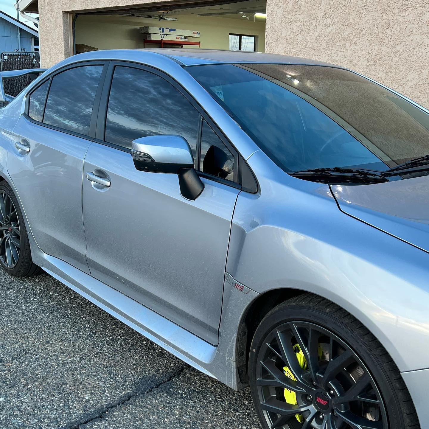 Silver Subaru WRX sedan with black rims, yellow brake calipers, tinted windows, parked outside a building.