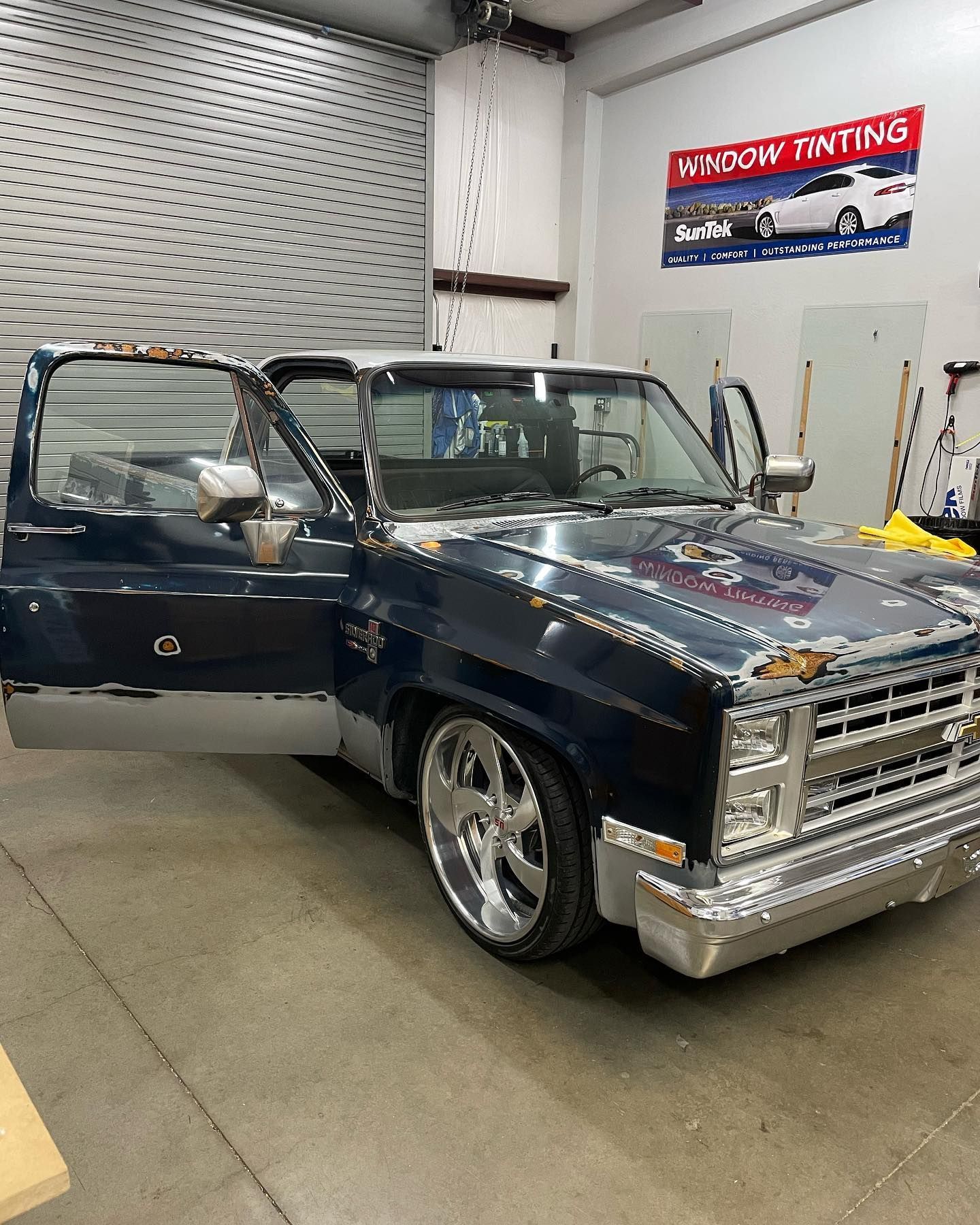 Blue customized Chevrolet pickup truck in a garage with open doors. Chrome wheels, and 