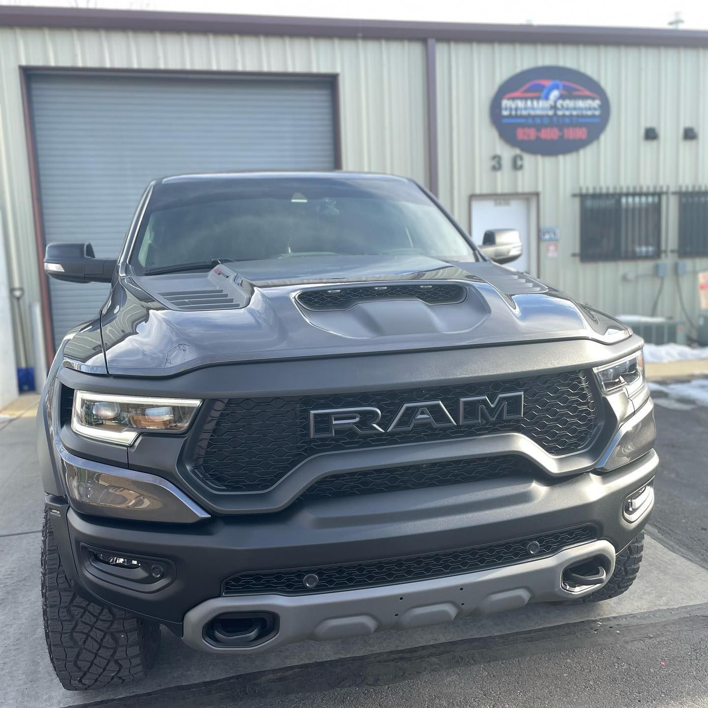 A dark gray Ram TRX truck parked in front of a building with a garage door.