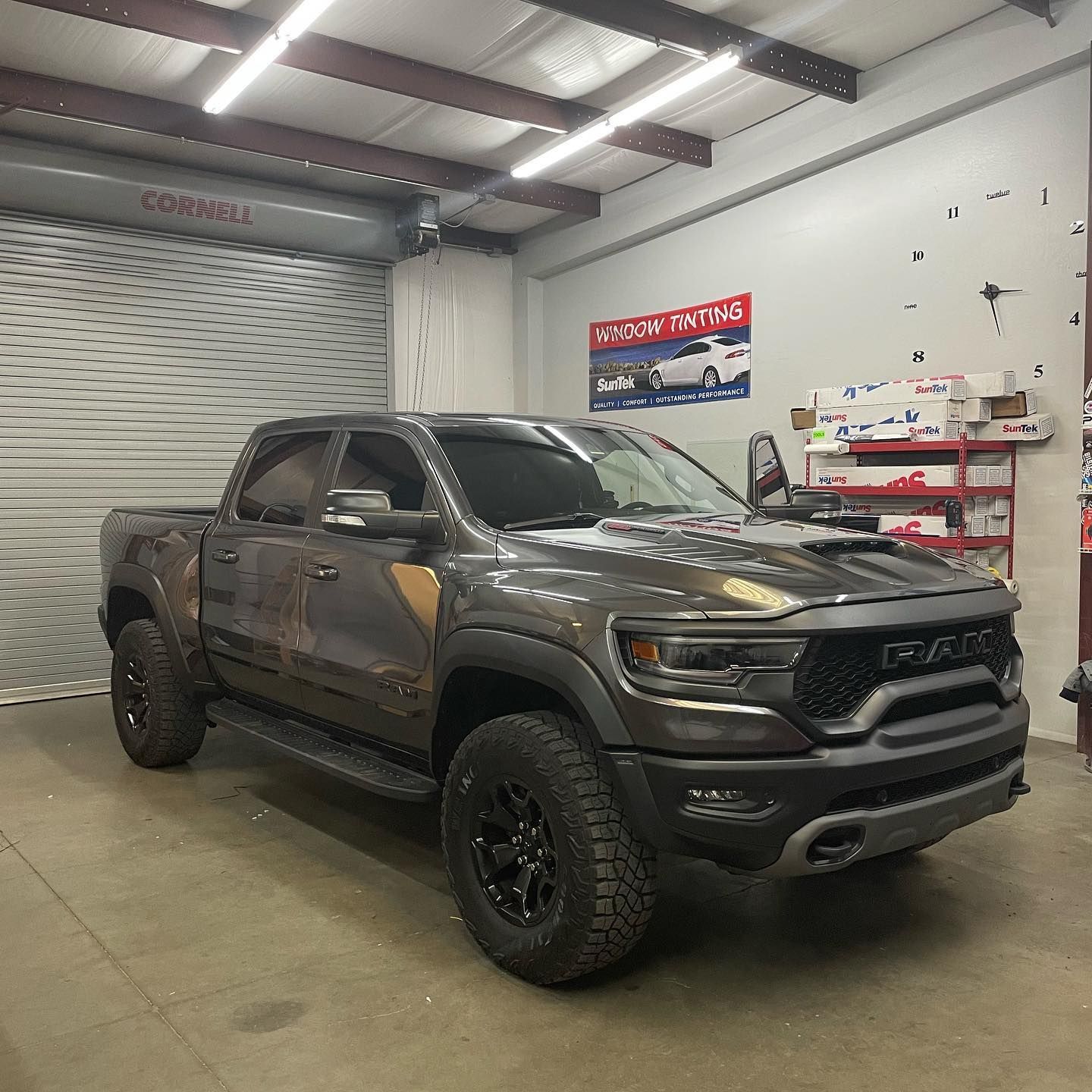 A grey RAM TRX truck with black wheels is parked in a garage. The vehicle has a wrap with a camouflage design.