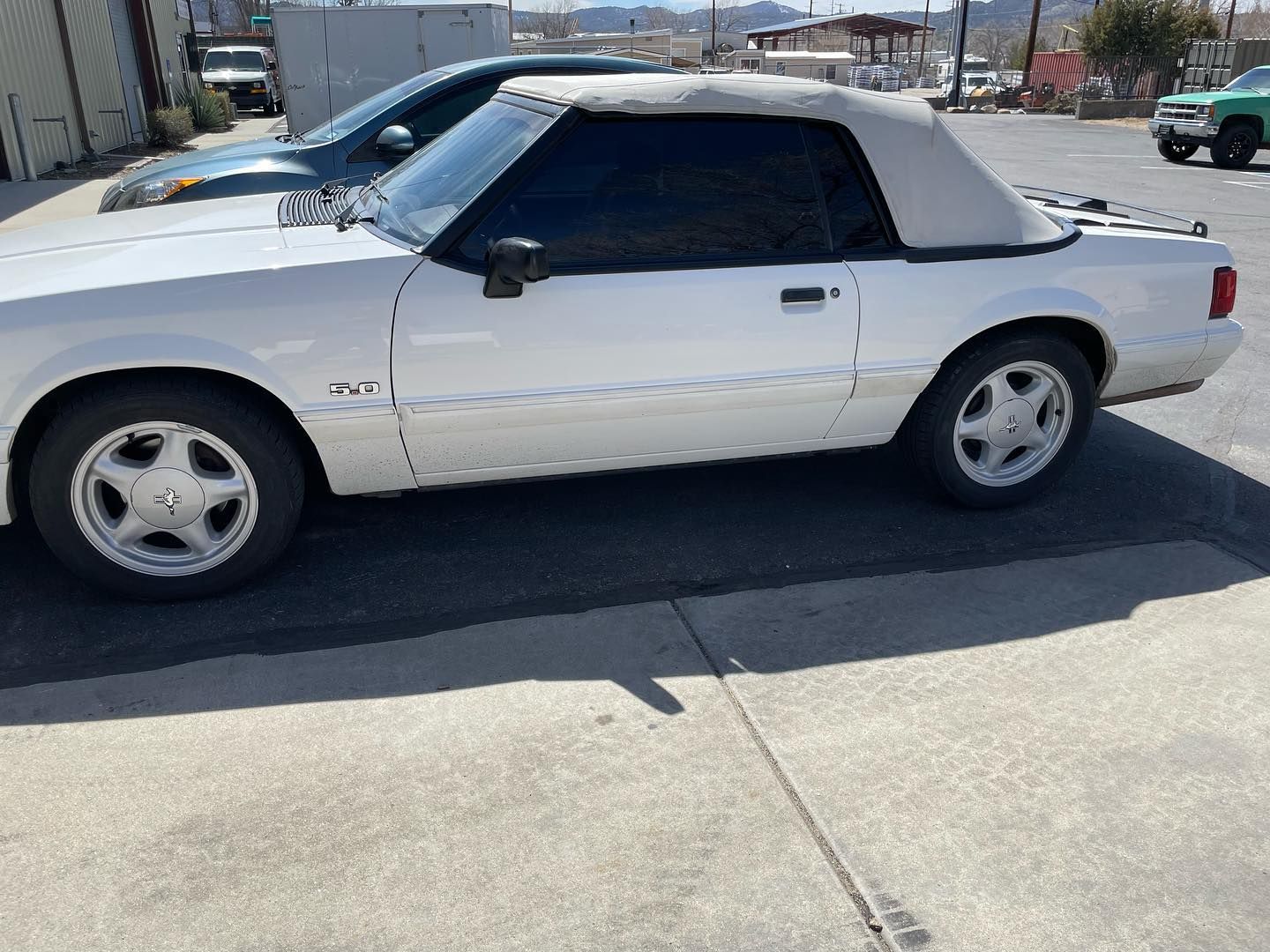White convertible Ford Mustang parked on asphalt, with a tan convertible top and tinted windows.