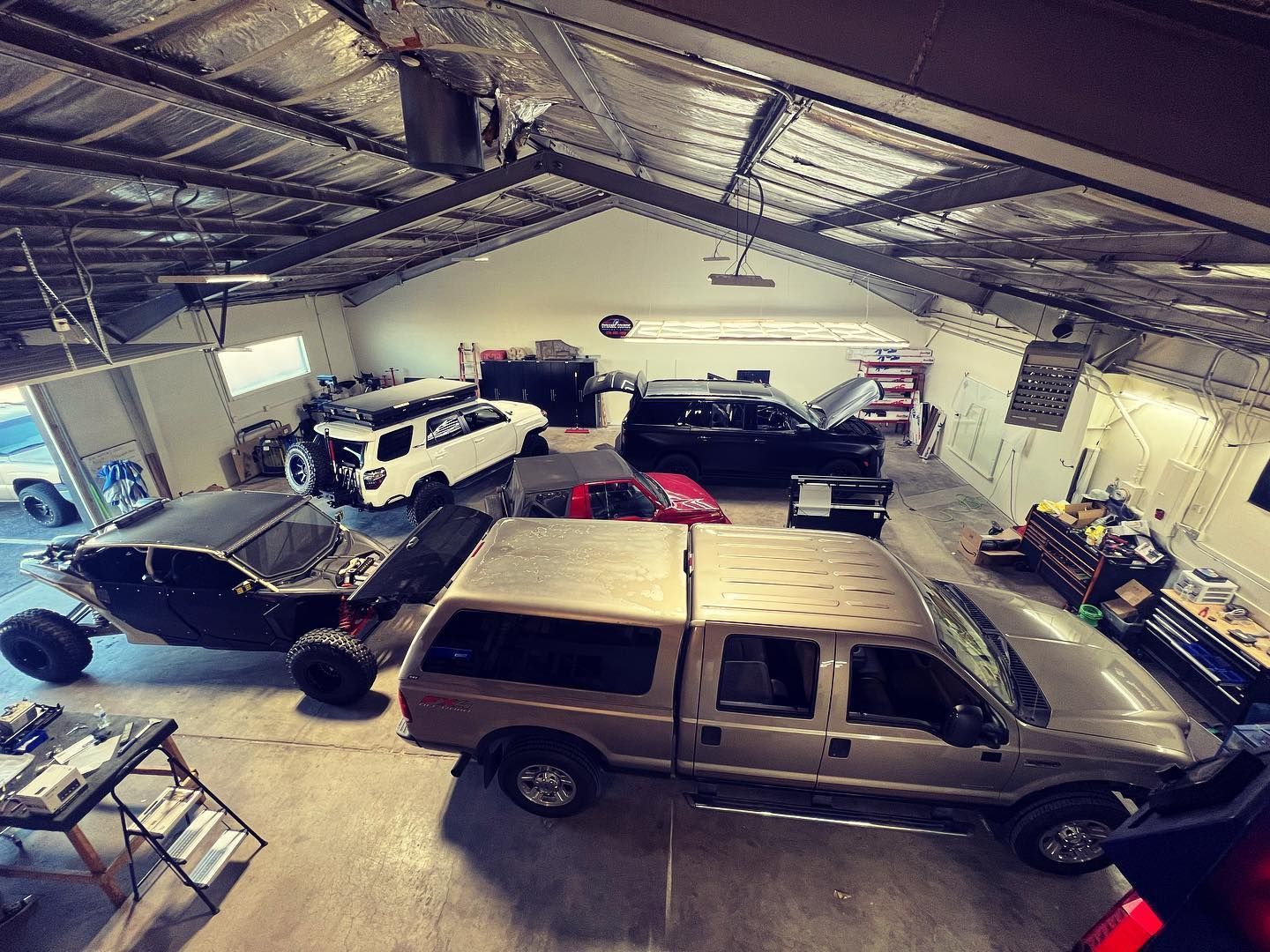 Overhead view of a spacious garage with several vehicles: a sand rail, truck, SUV, and others.