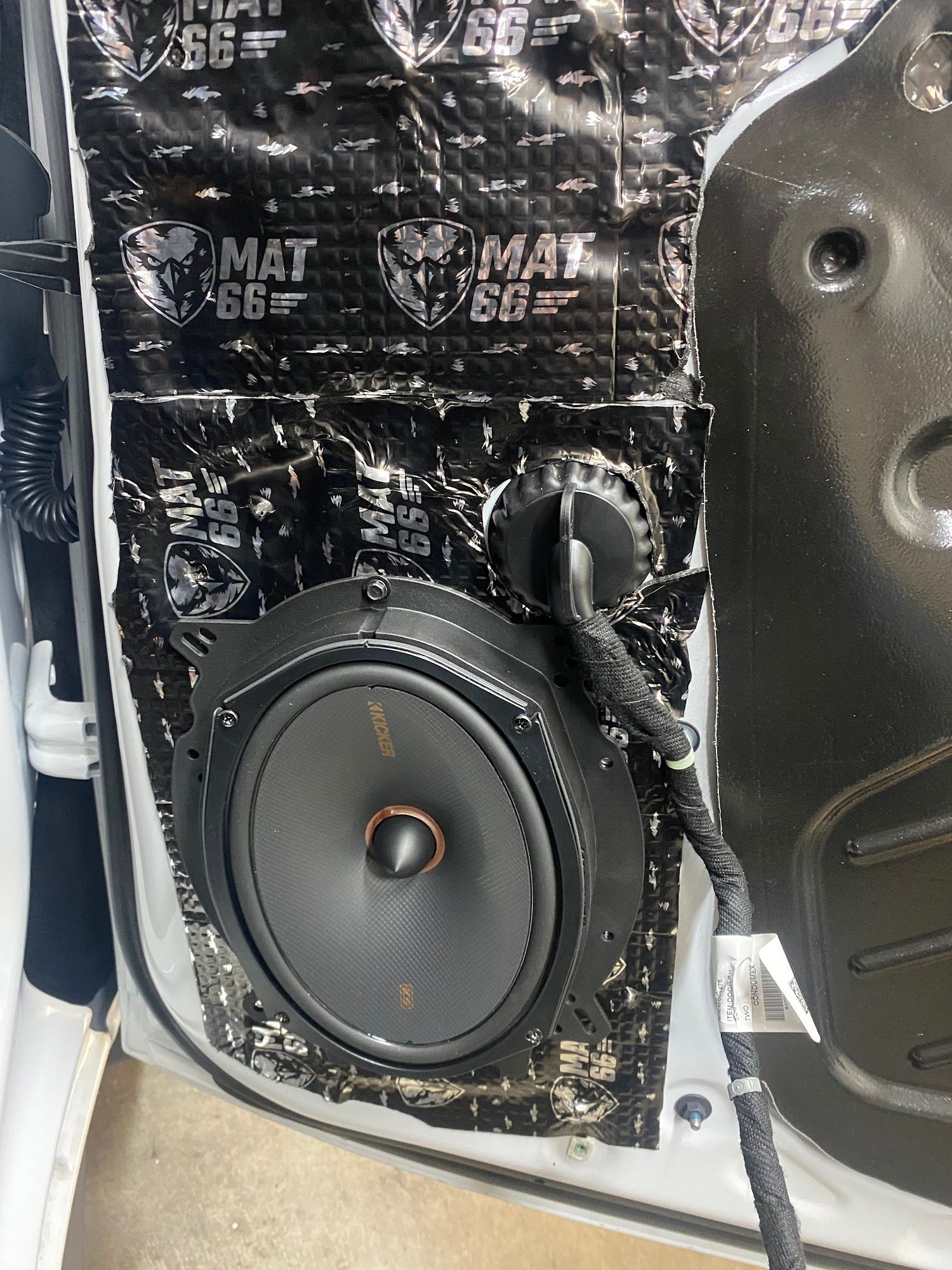 Car door interior with speaker installed. Black sound-dampening material covers the door's interior, with a black speaker at the center.