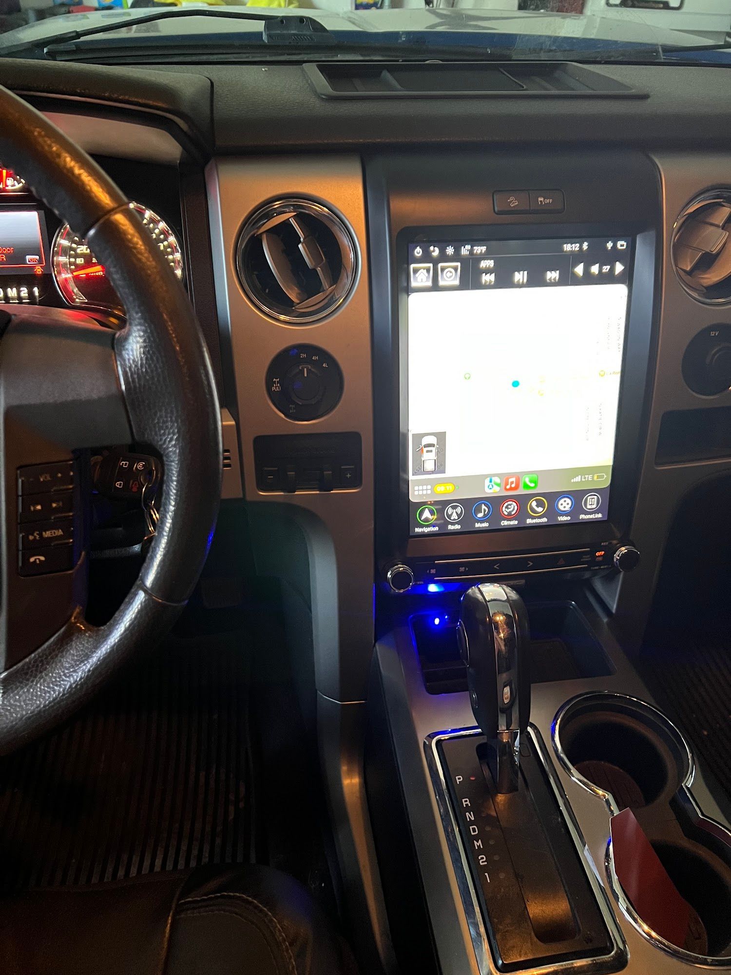 Interior view of a car's dashboard featuring a large touchscreen display, steering wheel, and gear shift. Silver and black interior, with blue accent lighting.