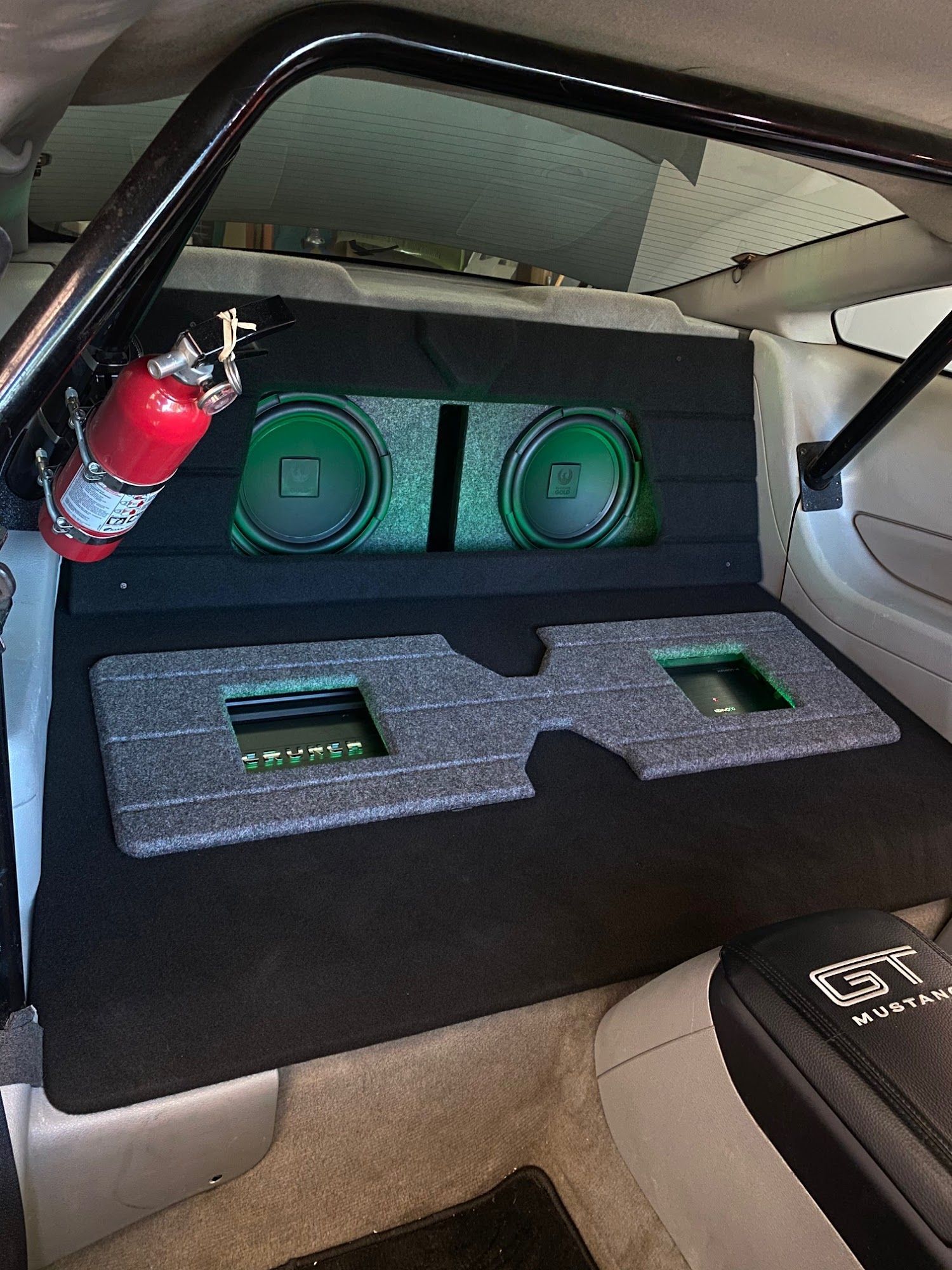Custom car audio setup in a vehicle's back seat area, featuring speakers, an amplifier, and a fire extinguisher.
