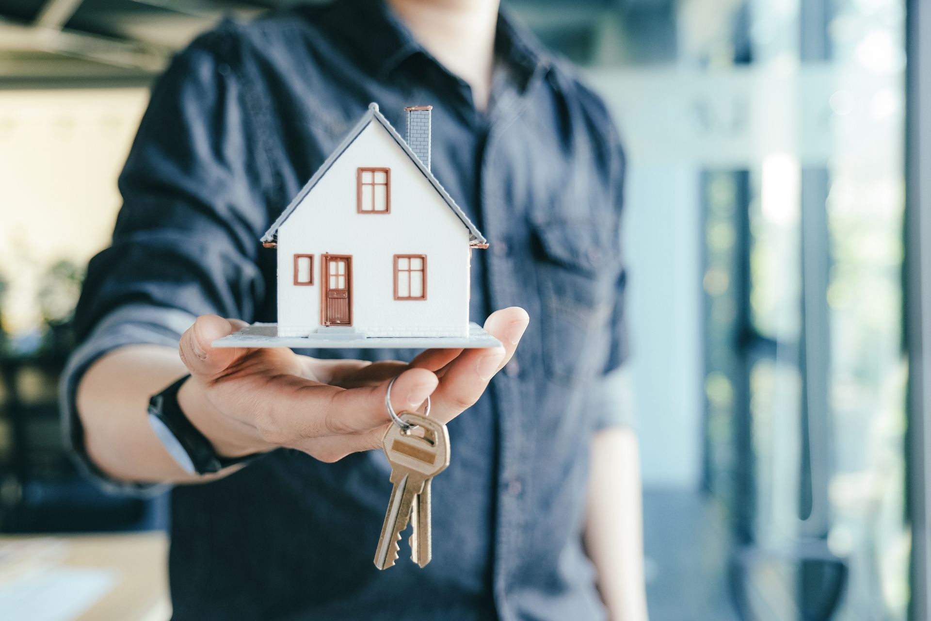 Person holding a small model house and keys, symbolizing rental property. Person holding a small model house and keys, symbolizing rental property.