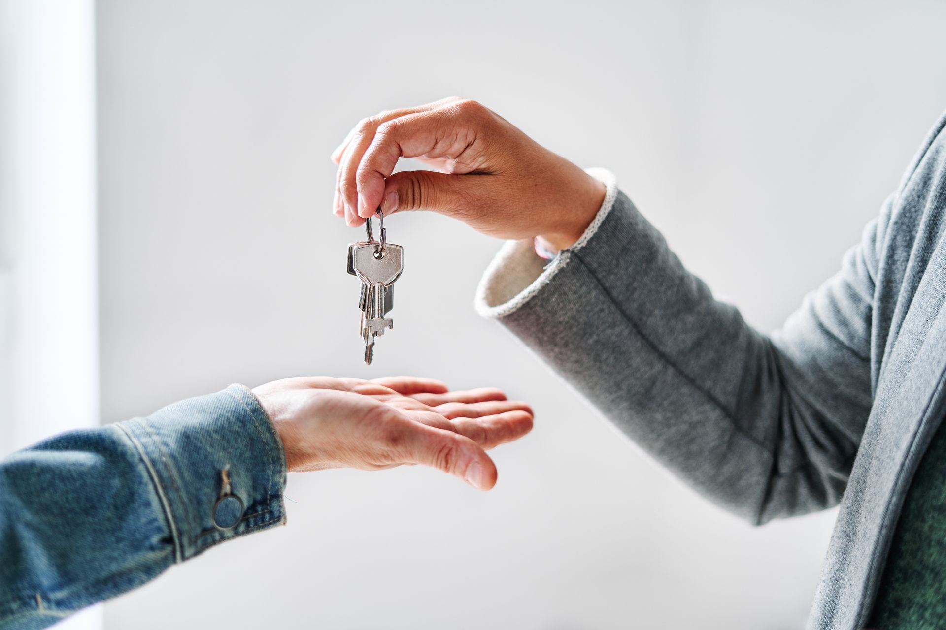 One person handing house keys to another person's open hand.