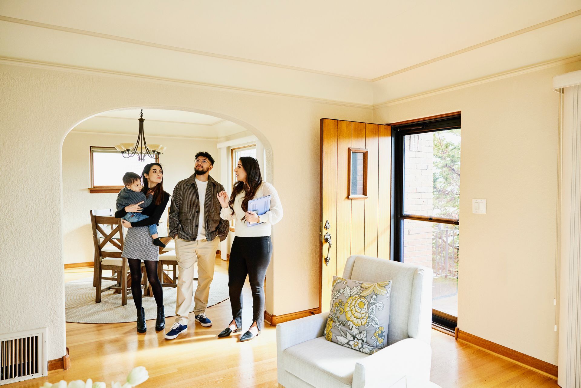 Real estate agent showing a family, including a child, a home's interior with an arched doorway.