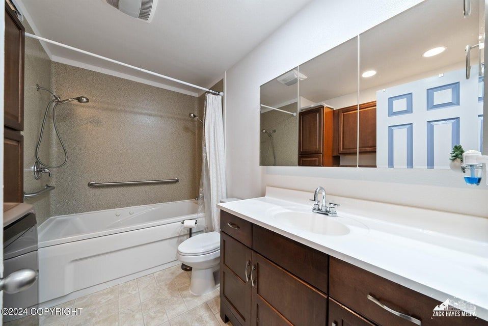 Bathroom with white sink, dark brown cabinets, tub/shower combo with grab bar, and large mirror.