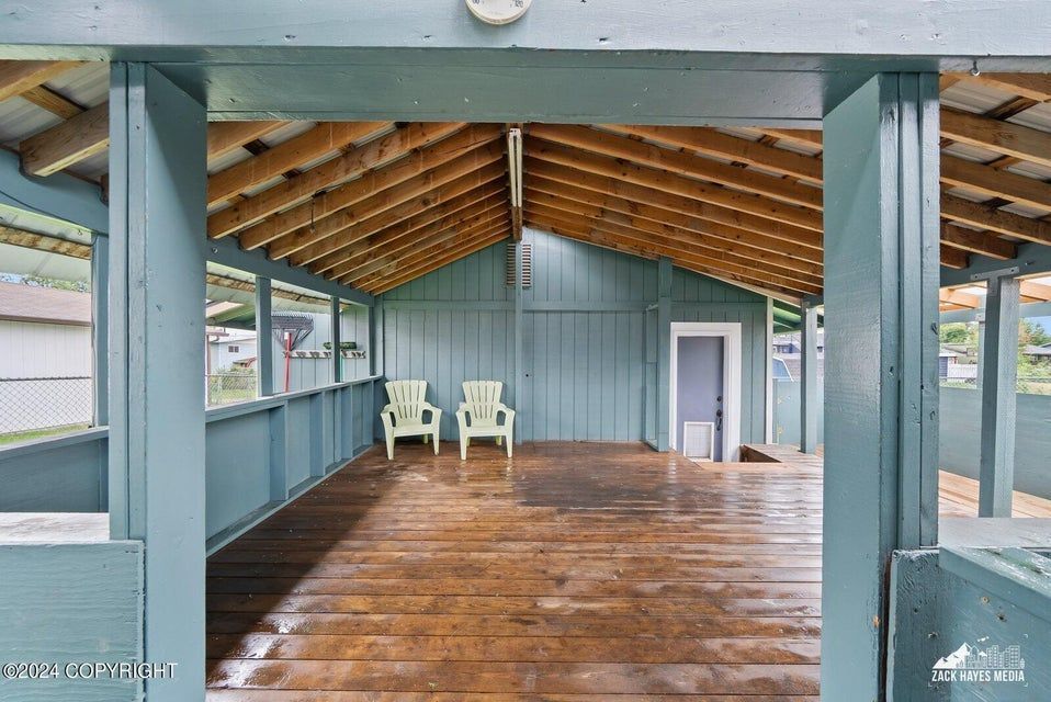 Blue wooden deck with two white chairs, under a covered porch.
