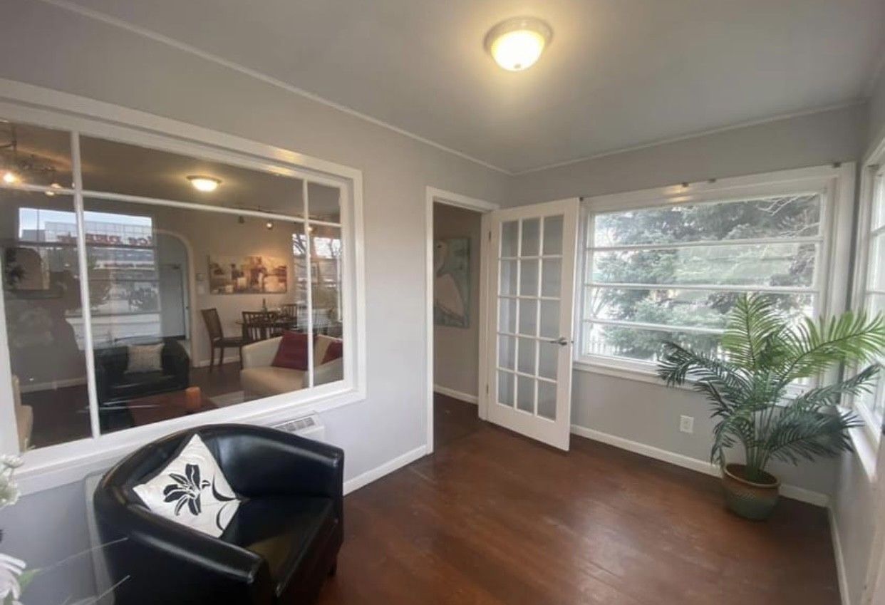 Sunroom with a black chair, hardwood floors, large windows, and a potted plant.
