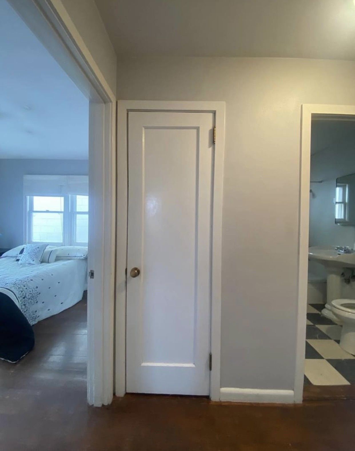 Hallway with closed white door, doorway to bedroom on the left, bathroom on the right.
