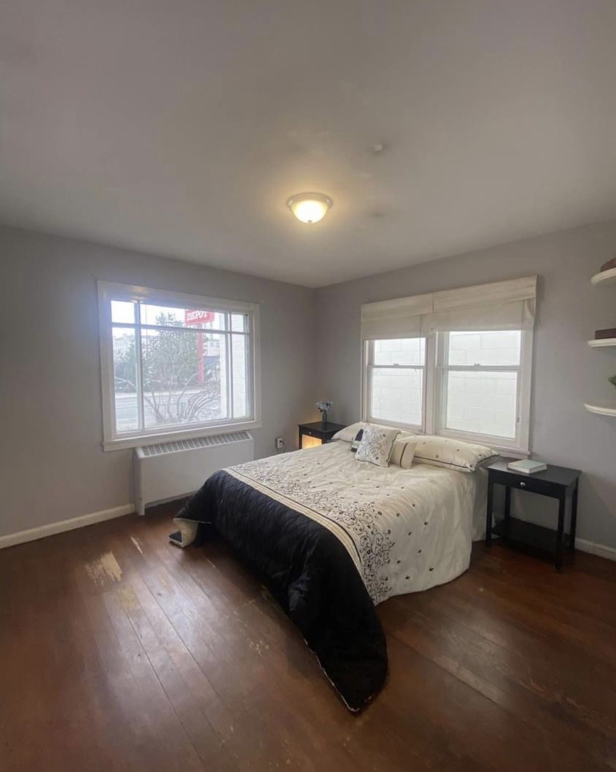 Bedroom with a bed, windows, nightstands, and hardwood floors. Gray walls, white comforter, dark blanket.