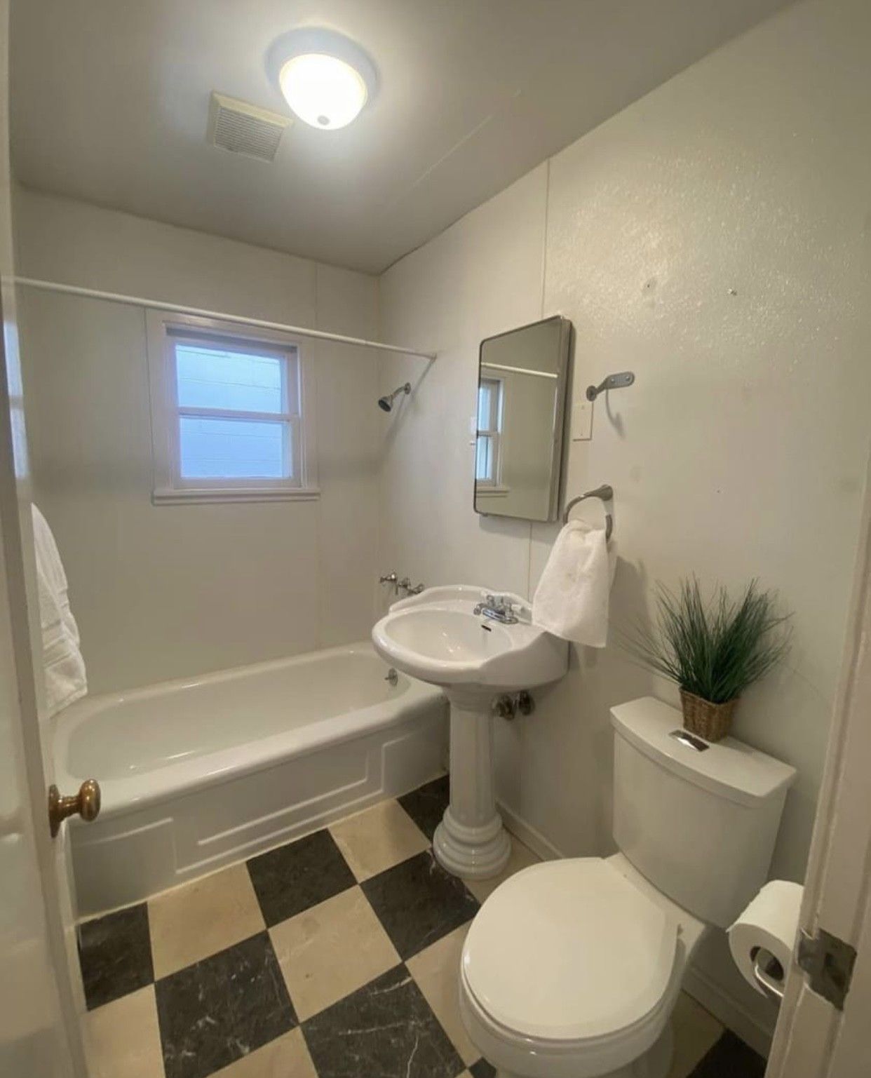 Bathroom with white fixtures, checkered floor, small window, and a towel.
