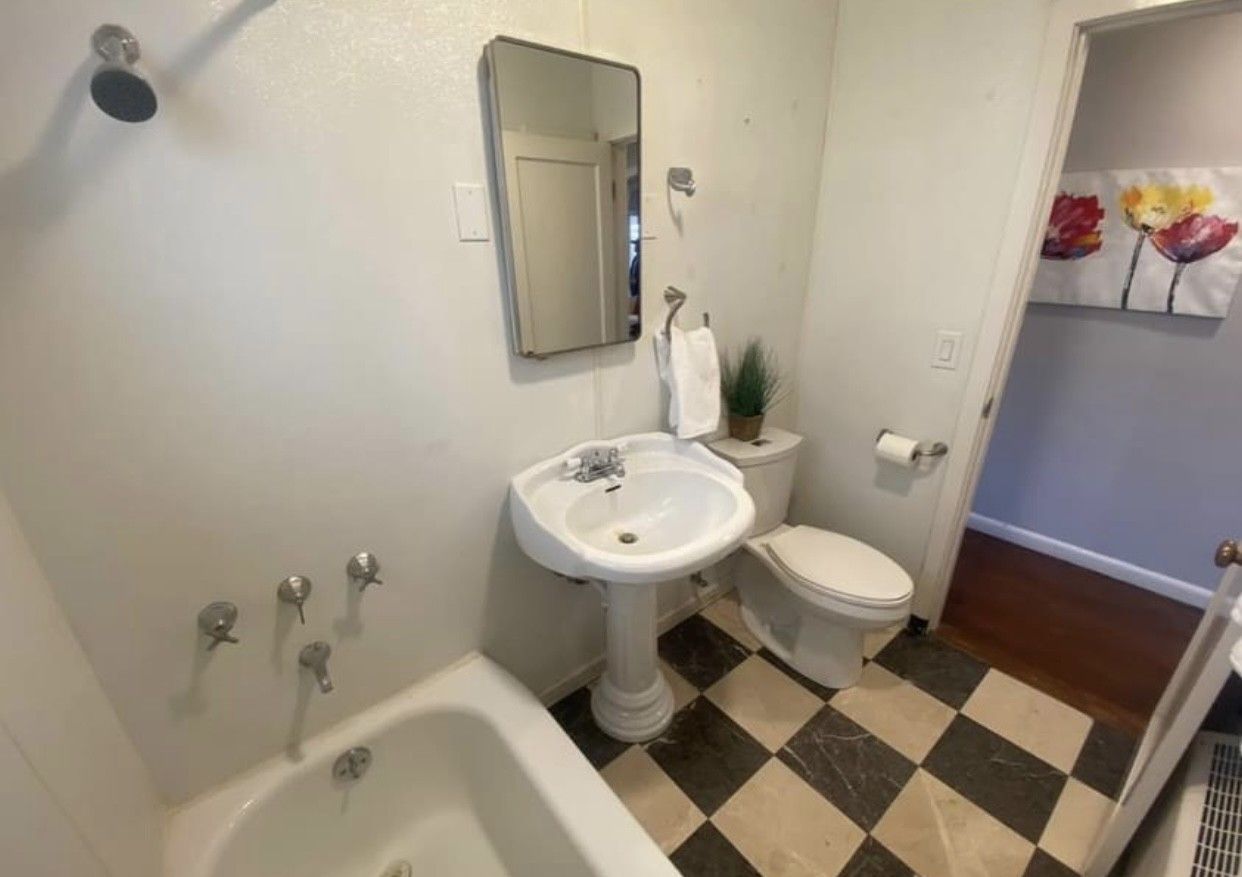 Bathroom with checkered floor, pedestal sink, toilet, tub, shower, and mirror.