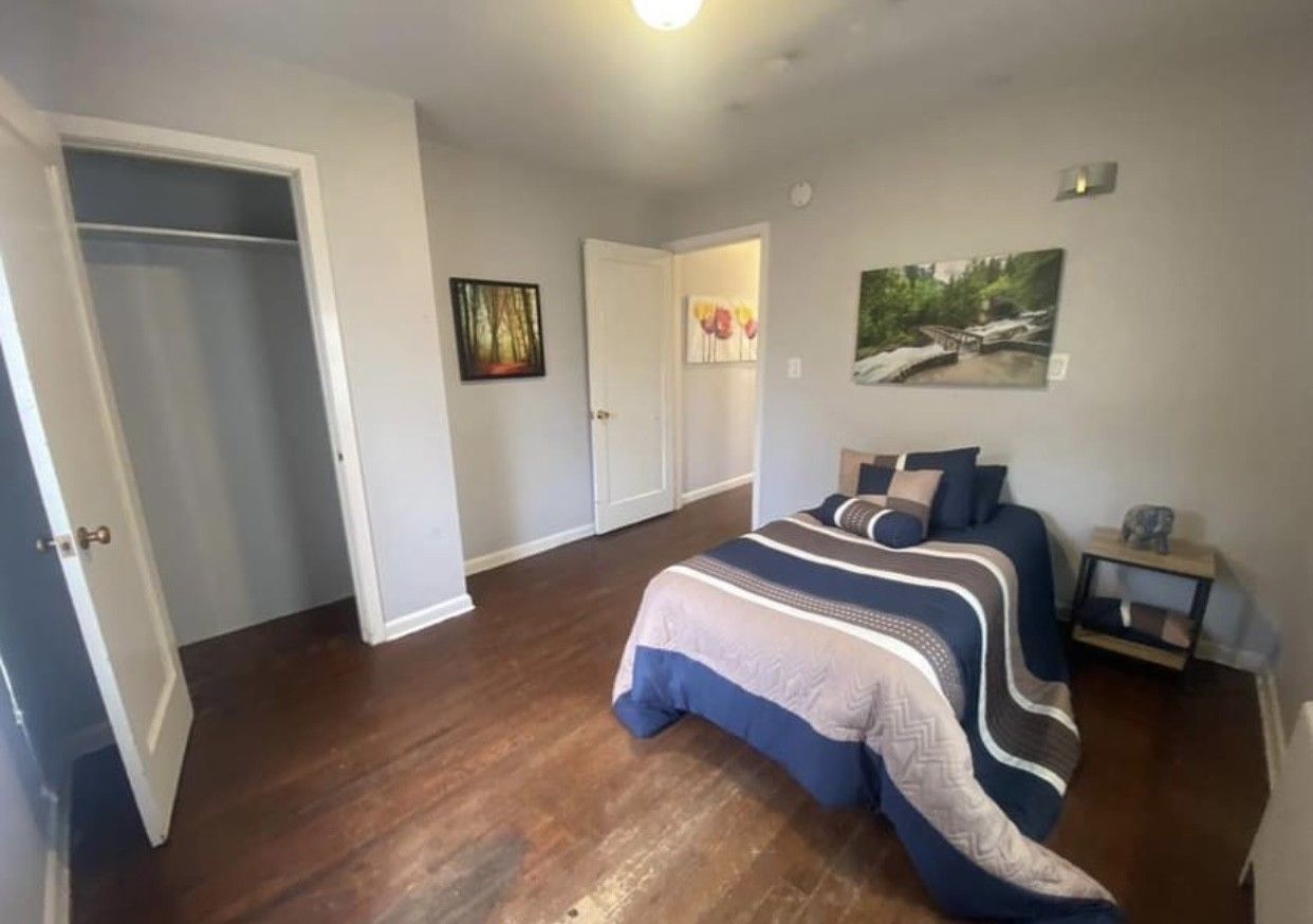Bedroom with bed, closet, artwork, and dark wood floors. Gray walls, blue and gray bedding.