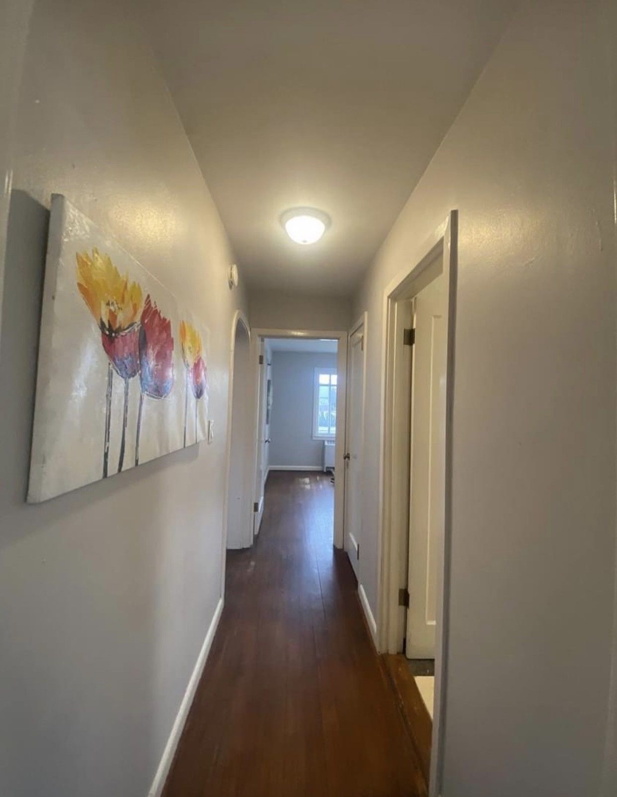 Long hallway with wood floor, white walls, and colorful art.