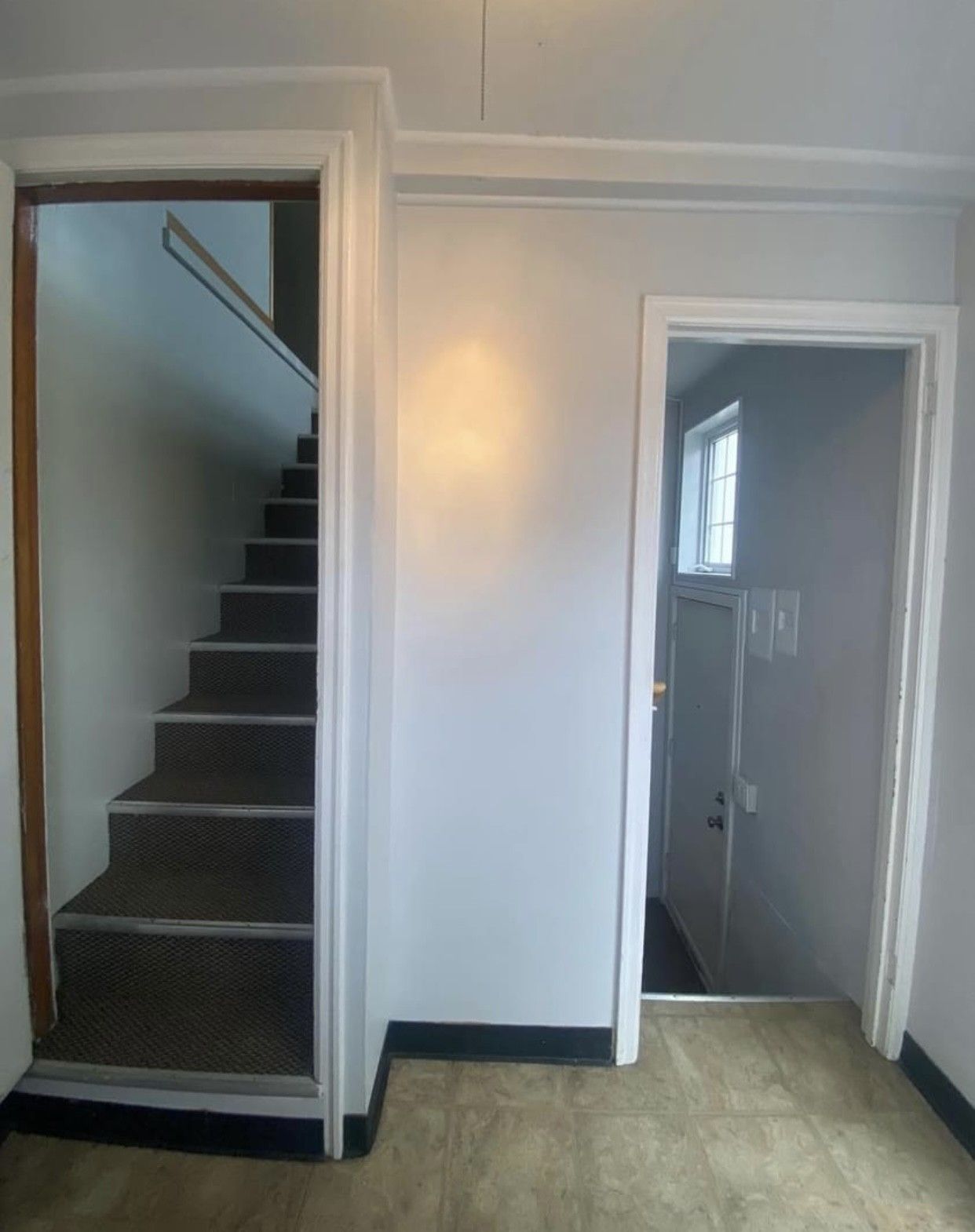 Hallway with stairs on the left, door on the right. Gray walls, brown carpet on stairs, tan floor.
