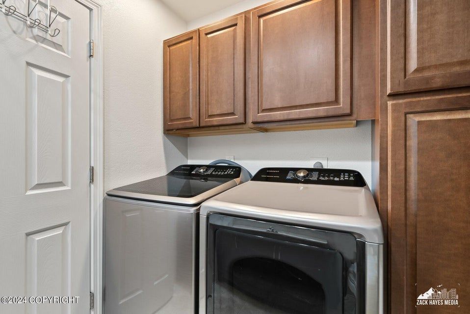 A laundry room with a washing machine, dryer, and cabinets. The room has a white door and walls.