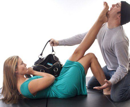 A woman in a blue dress is laying on the floor while a man holds her purse