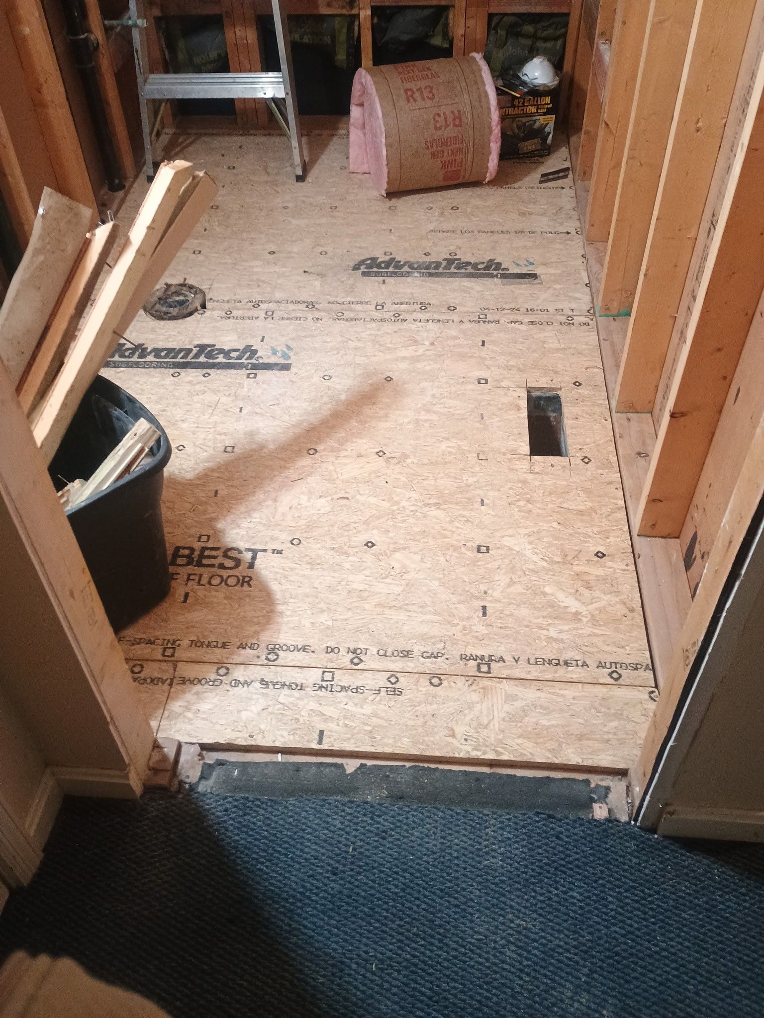 Partially finished hallway floor with exposed plywood, insulation, and construction materials along the walls
