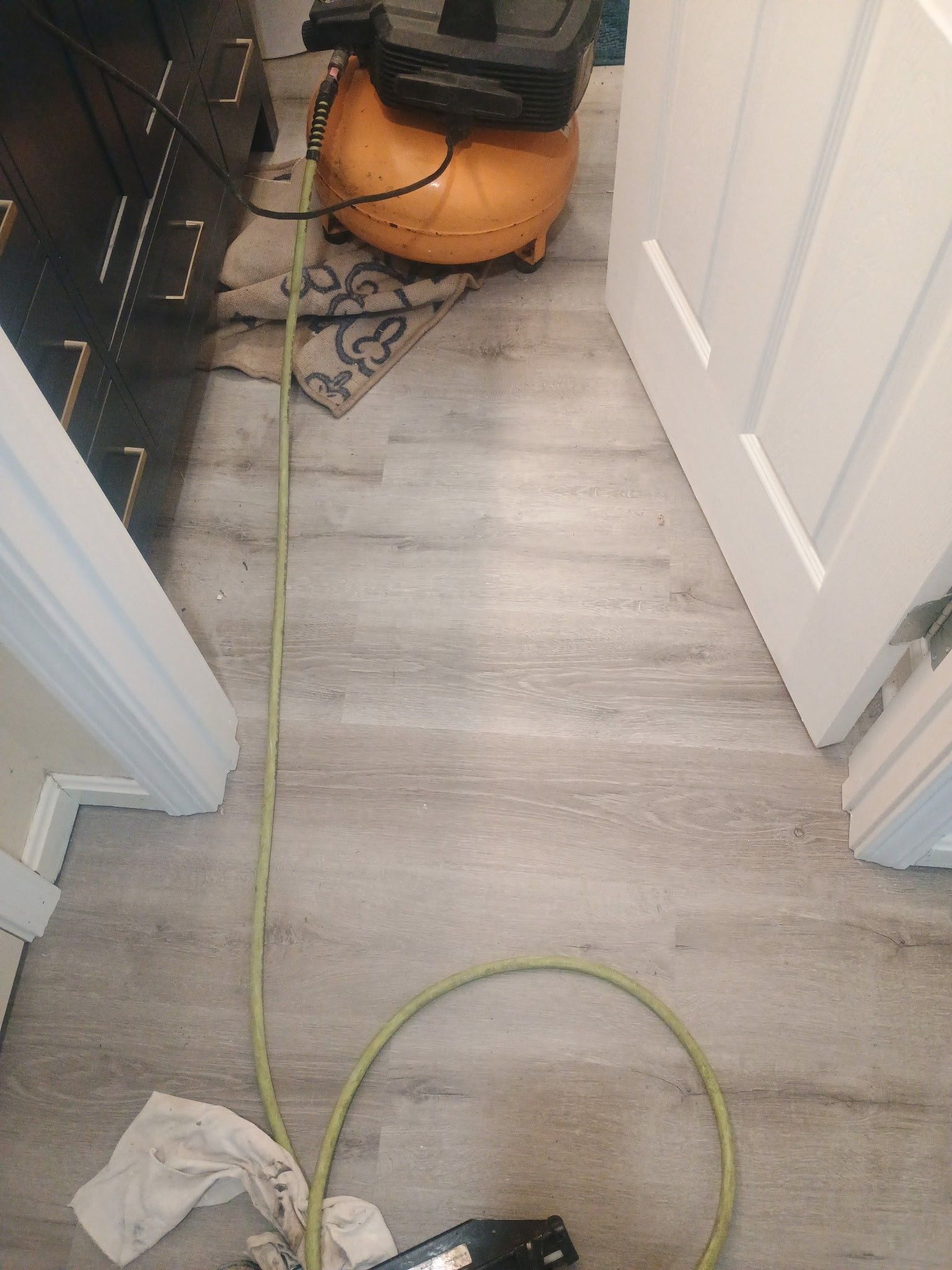 Cluttered hallway with a green cord, orange vacuum, and a white cloth on gray wood floor