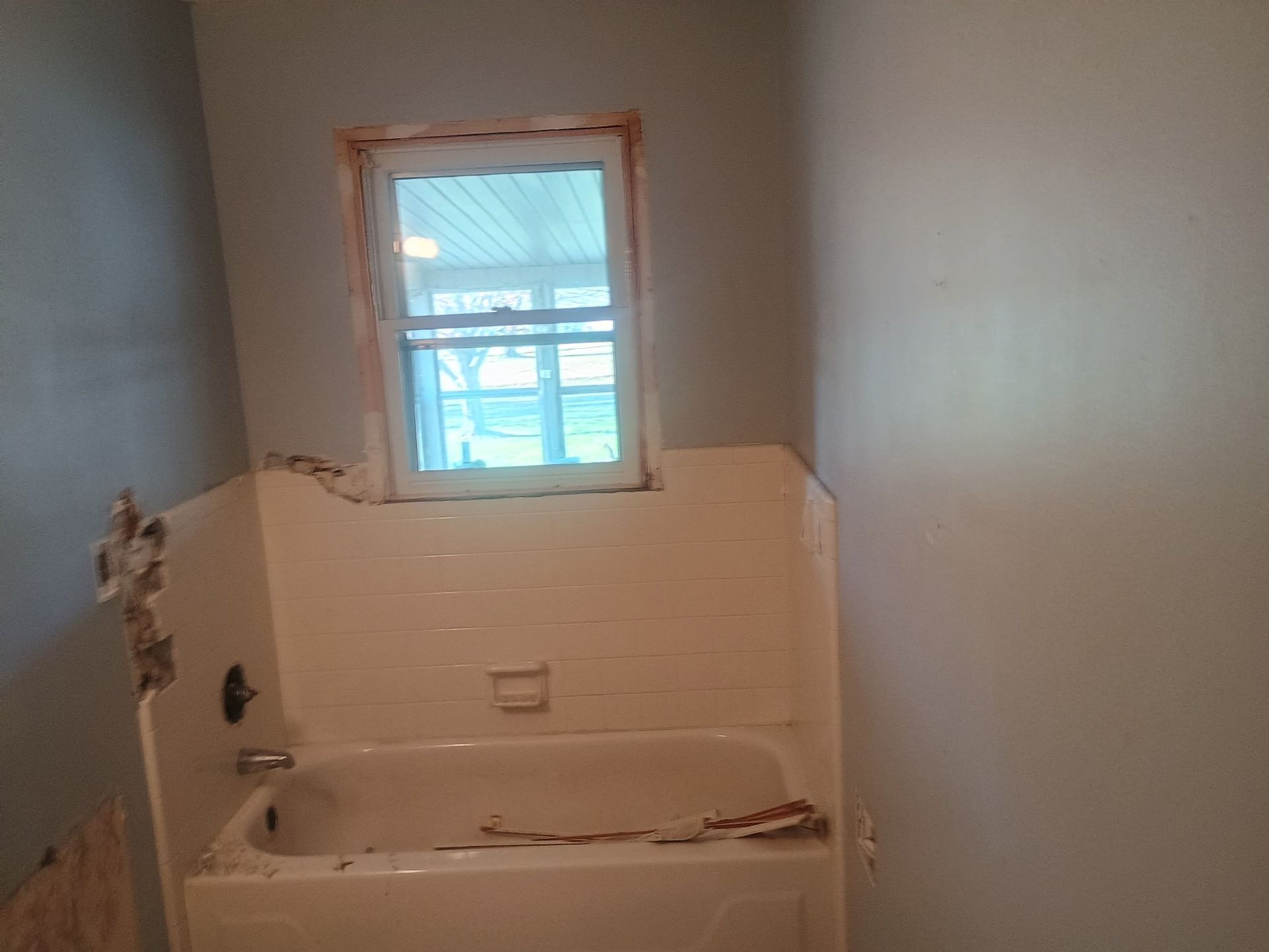 Small bathroom under renovation with a bathtub, exposed drywall, and a window above the tub.