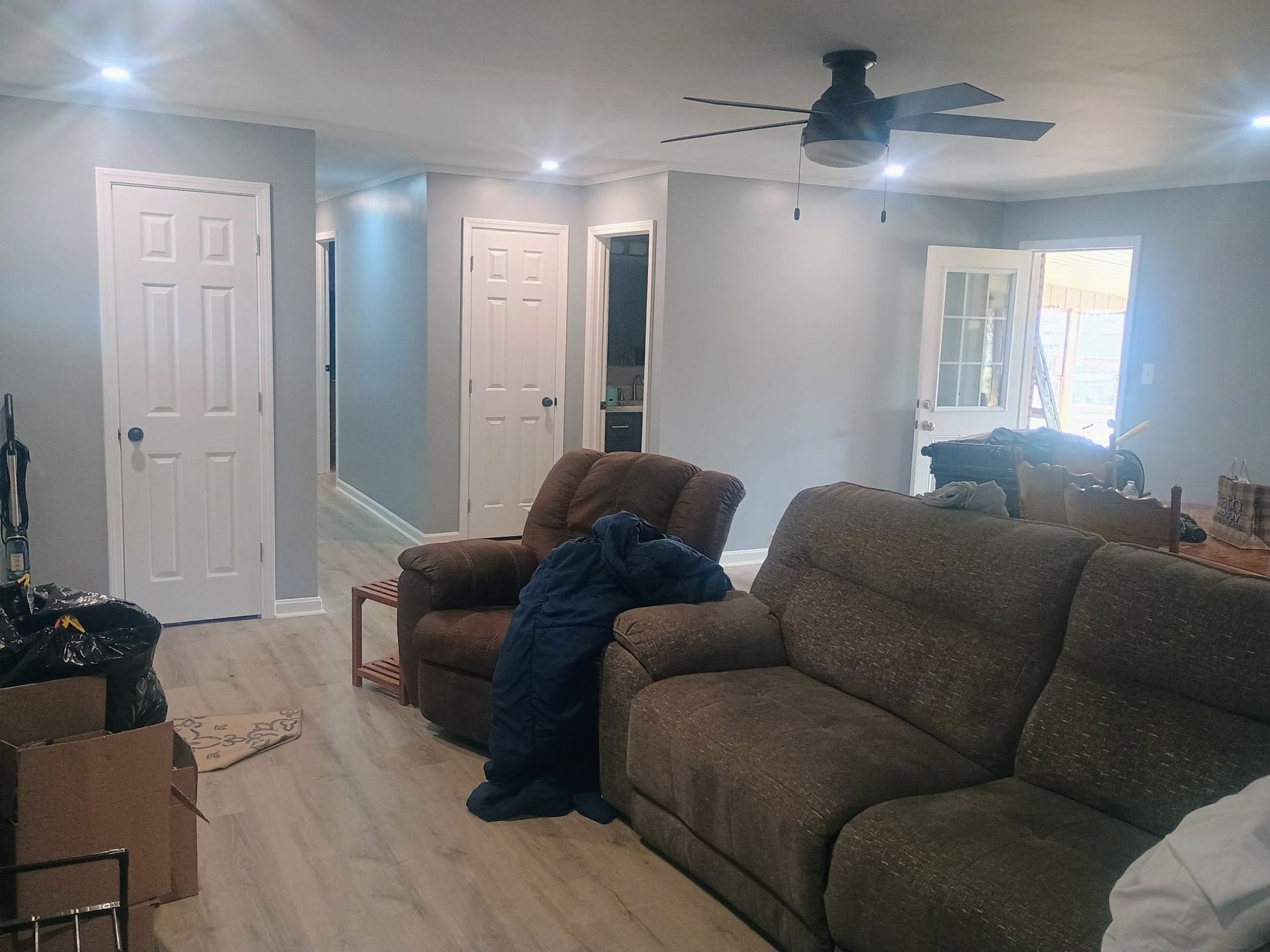 Living room with brown sofas, ceiling fan, white doors, and bright window light