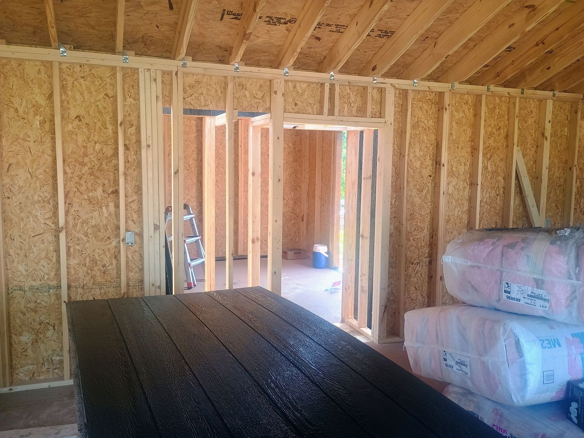 Unfinished interior with wood studs, open doorway, table, and stacked insulation rolls