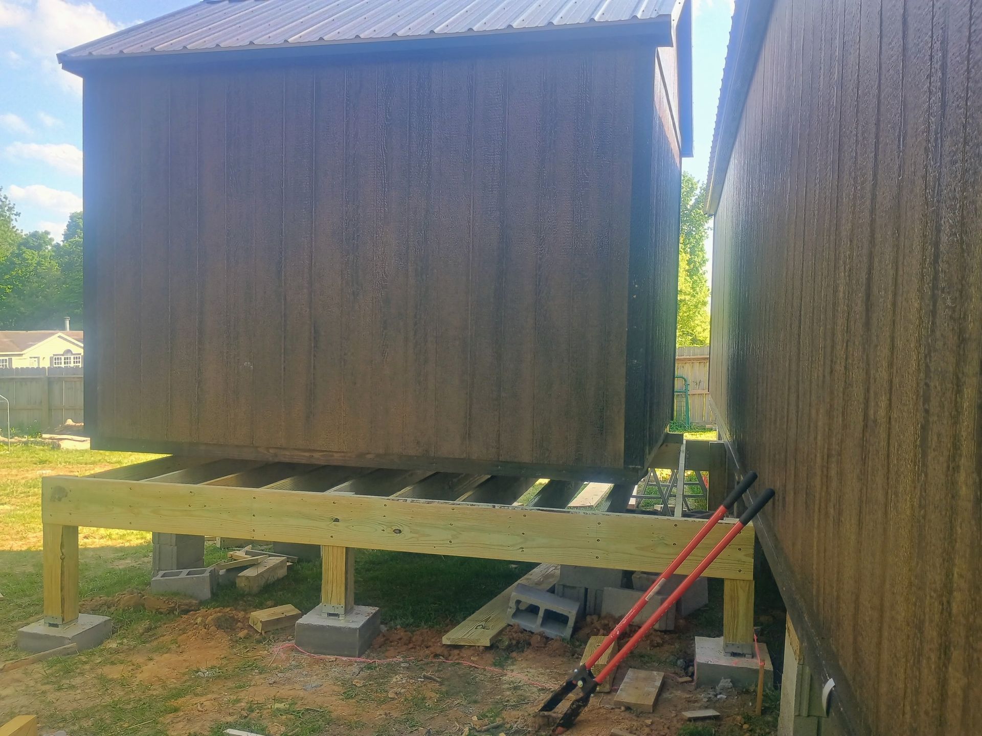 Two small wooden sheds raised on concrete blocks, with red ladders and a grassy yard around them.