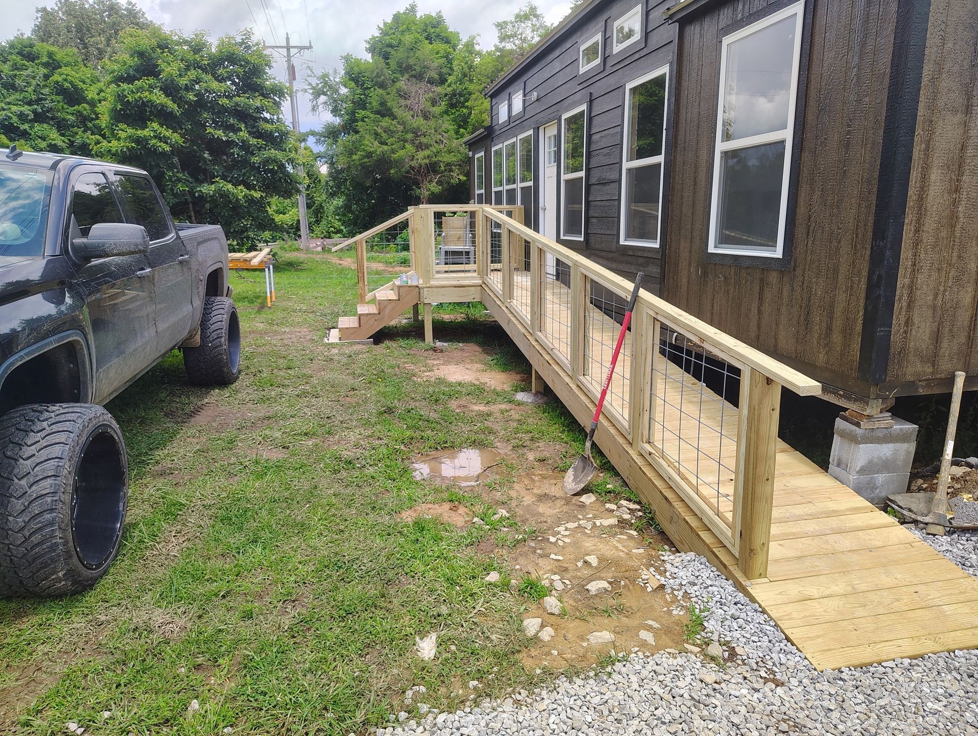 Raised wooden ramp beside a dark house, with a black truck parked on grass nearby.