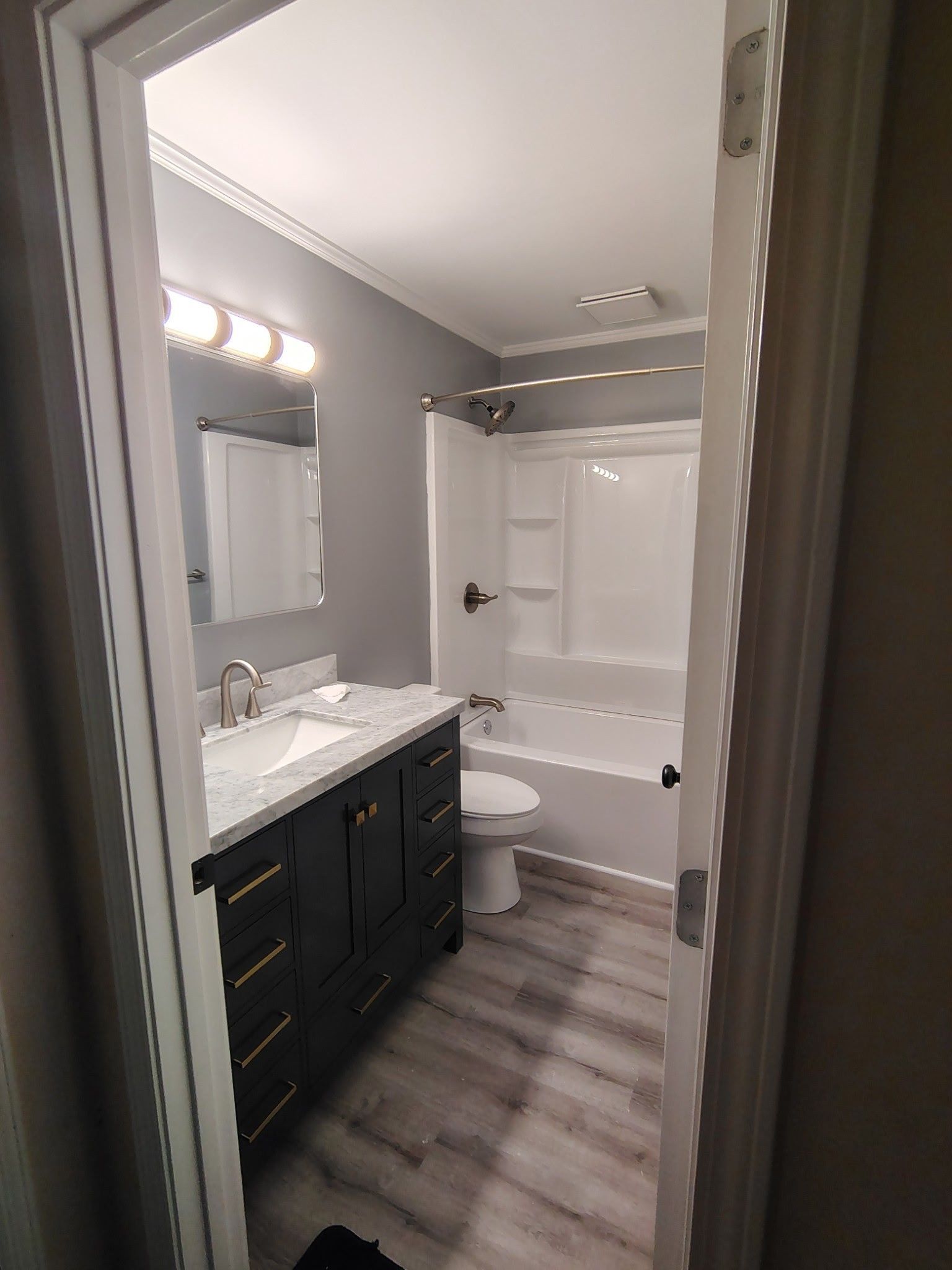 Small bathroom with black vanity, white tub-shower, and gray wood-look floor tiles
